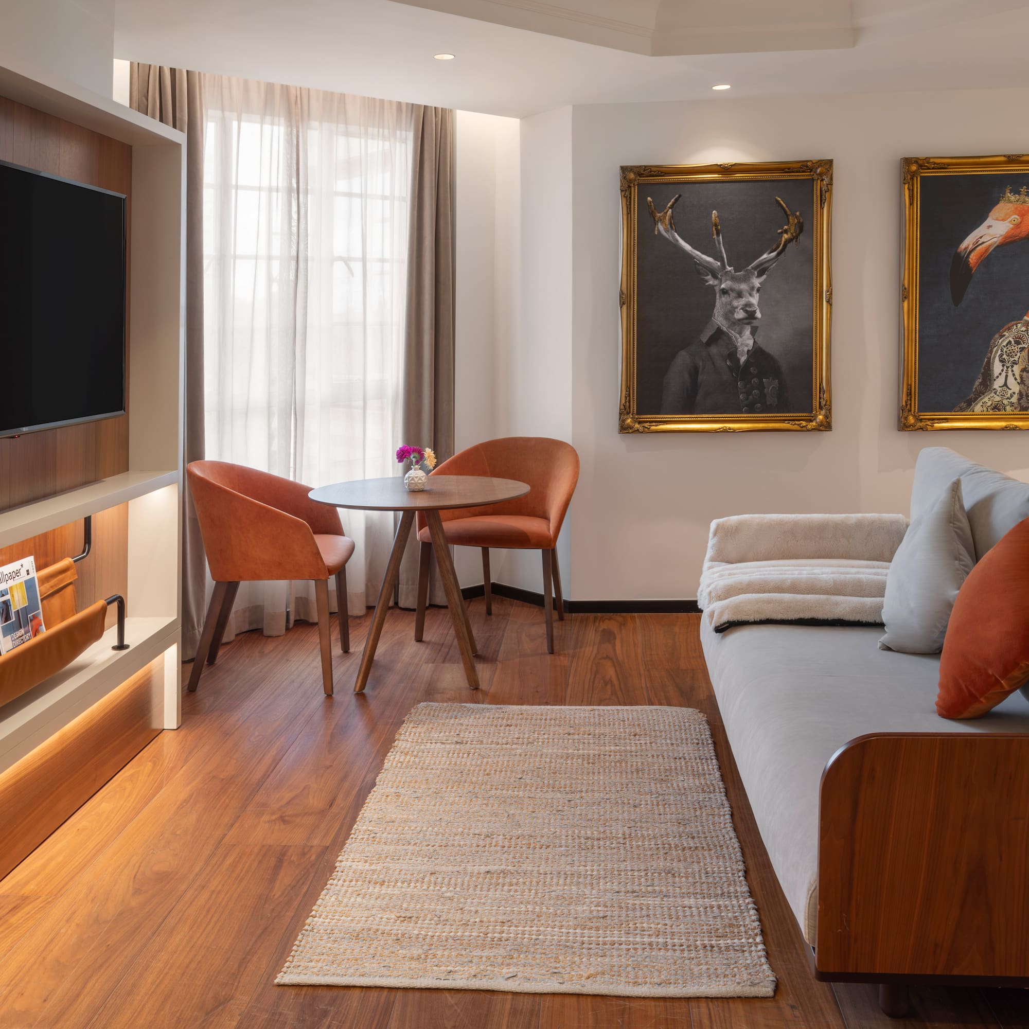Hotel suite living space with TV, sofa, dining area, and framed animal art.