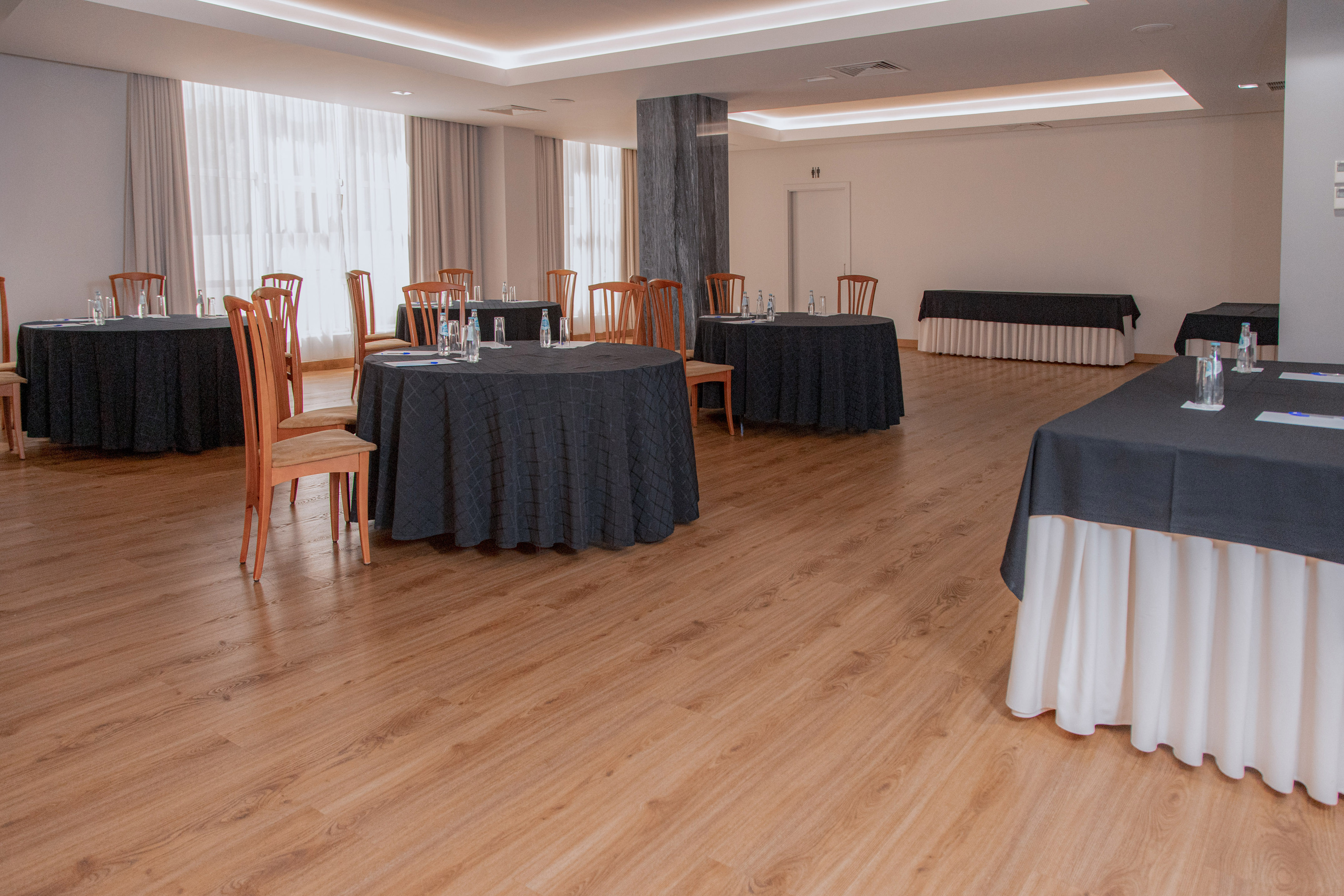 Meeting room setup with black round tables, wooden chairs, and wood floor.