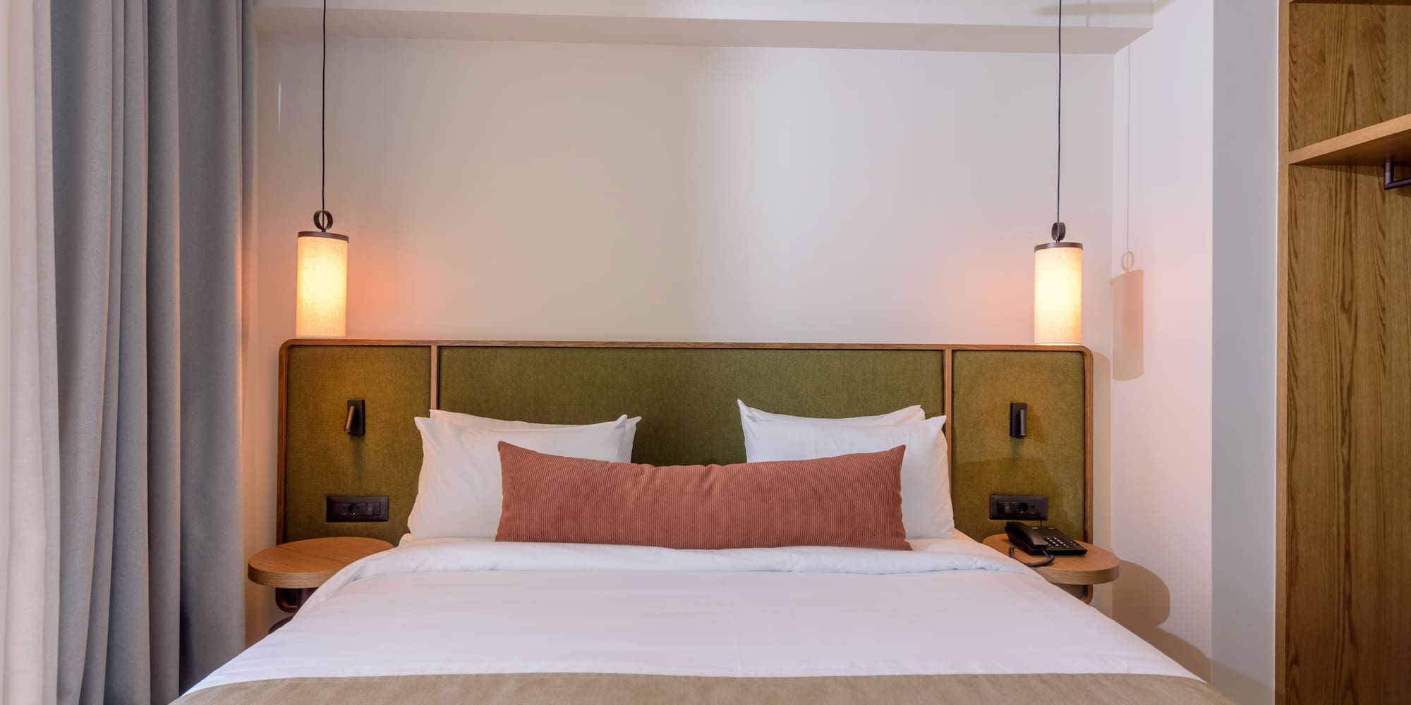 Hotel bedroom interior: cozy bed, green headboard, and modern pendant lights.