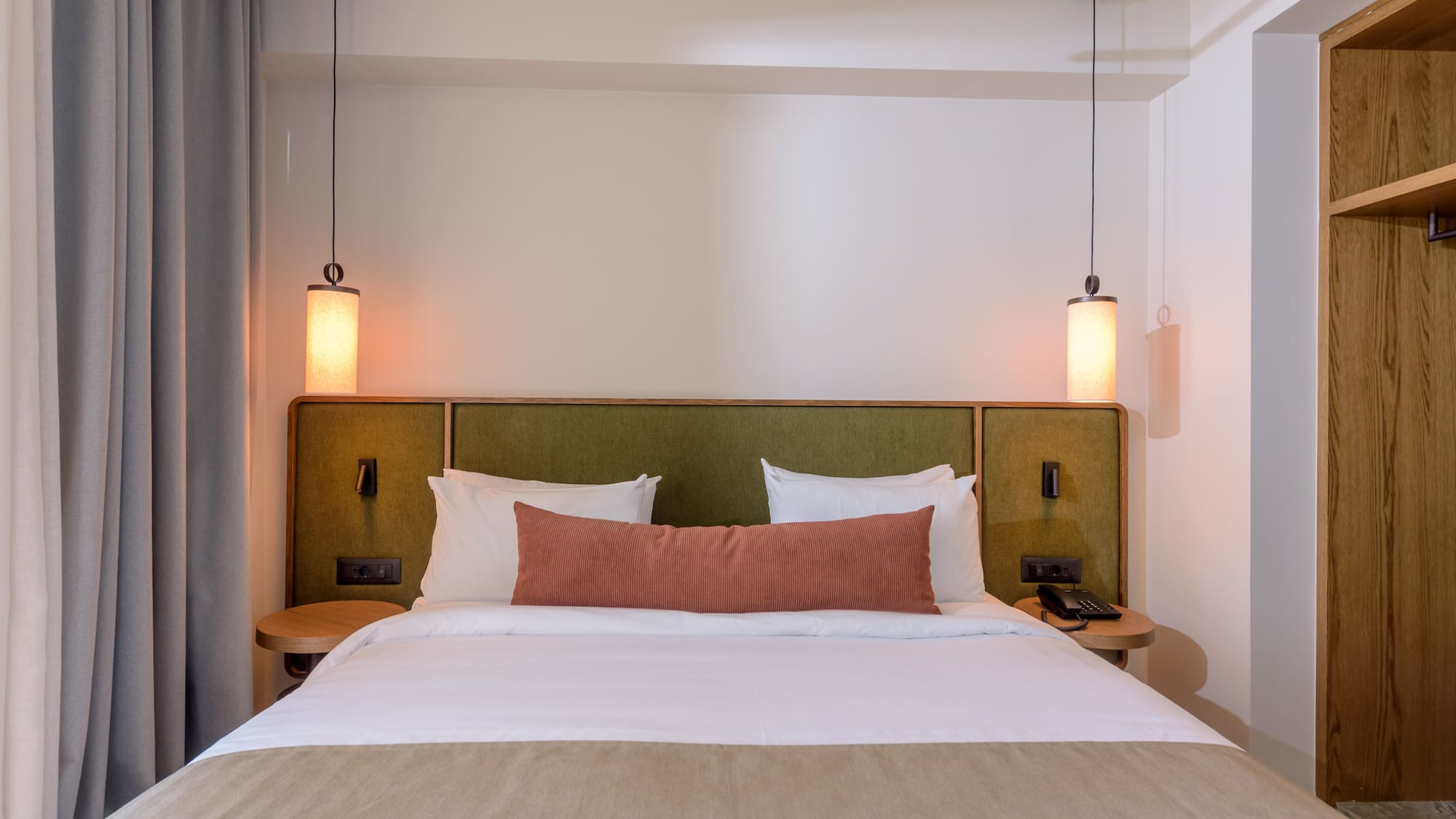 Hotel bedroom interior: cozy bed, green headboard, and modern pendant lights.