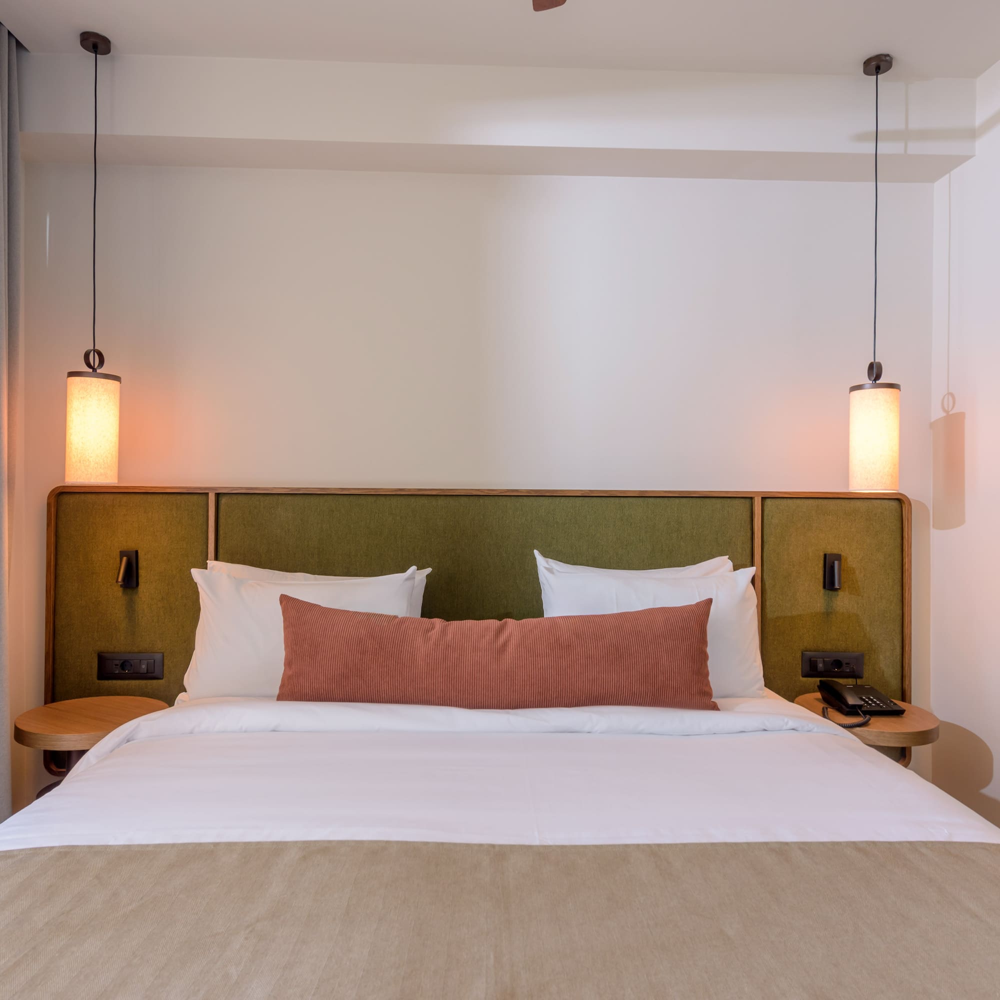 Hotel bedroom interior: cozy bed, green headboard, and modern pendant lights.