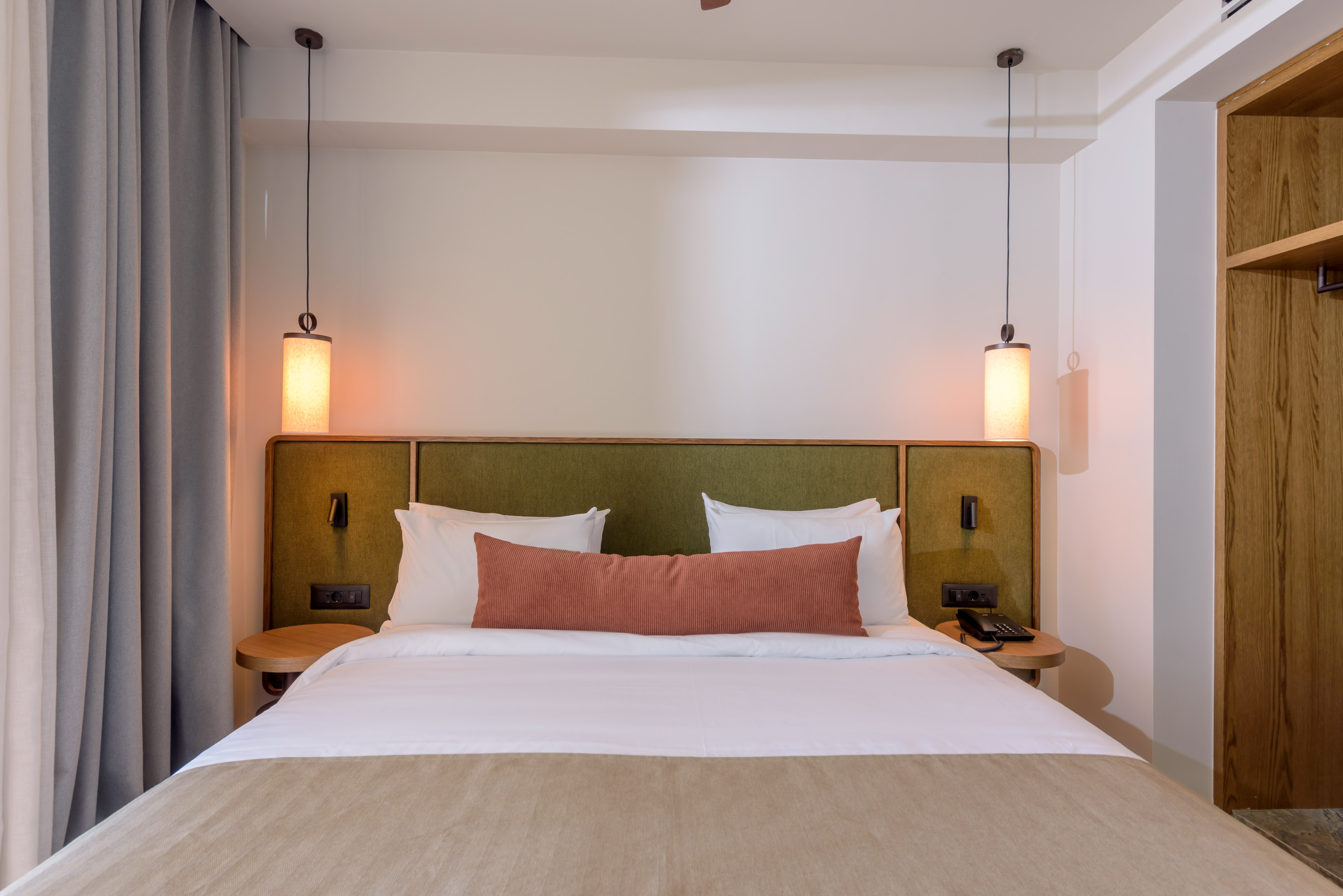 Hotel bedroom interior: cozy bed, green headboard, and modern pendant lights.