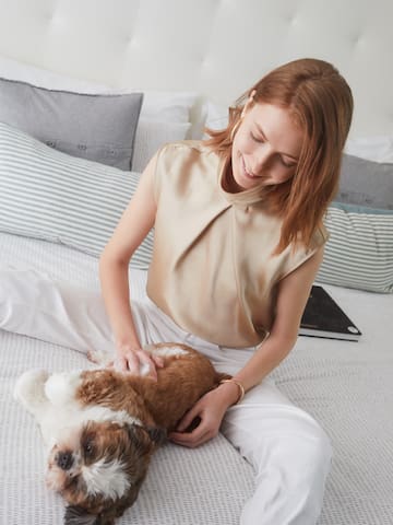 a woman sitting on a bed petting a dog