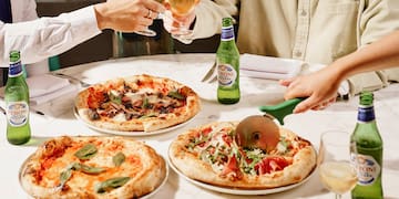 a group of people sitting at a table with pizzas and drinks