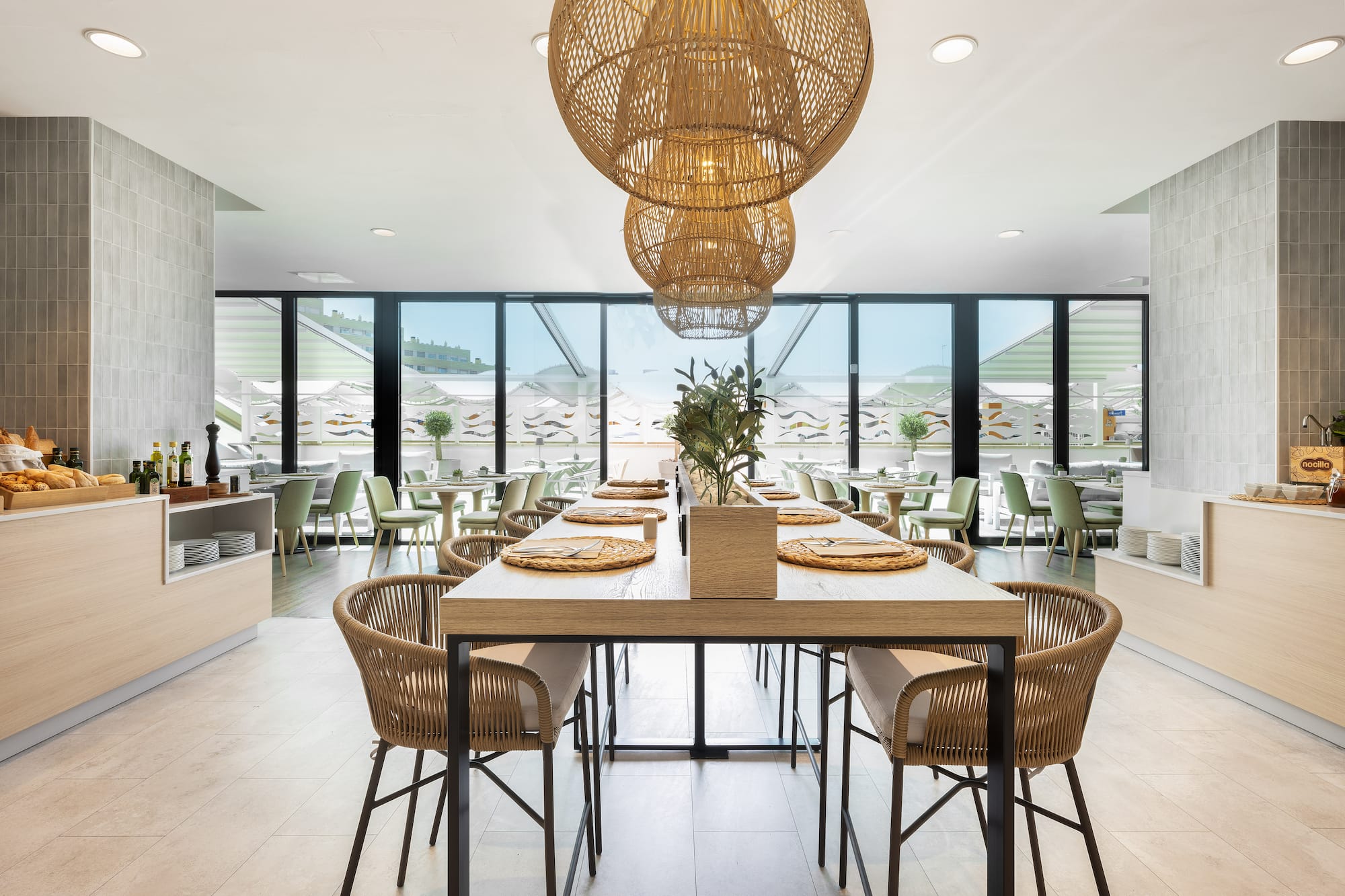 Comedor moderno de hotel con mesa larga, buffet y lámparas de mimbre.