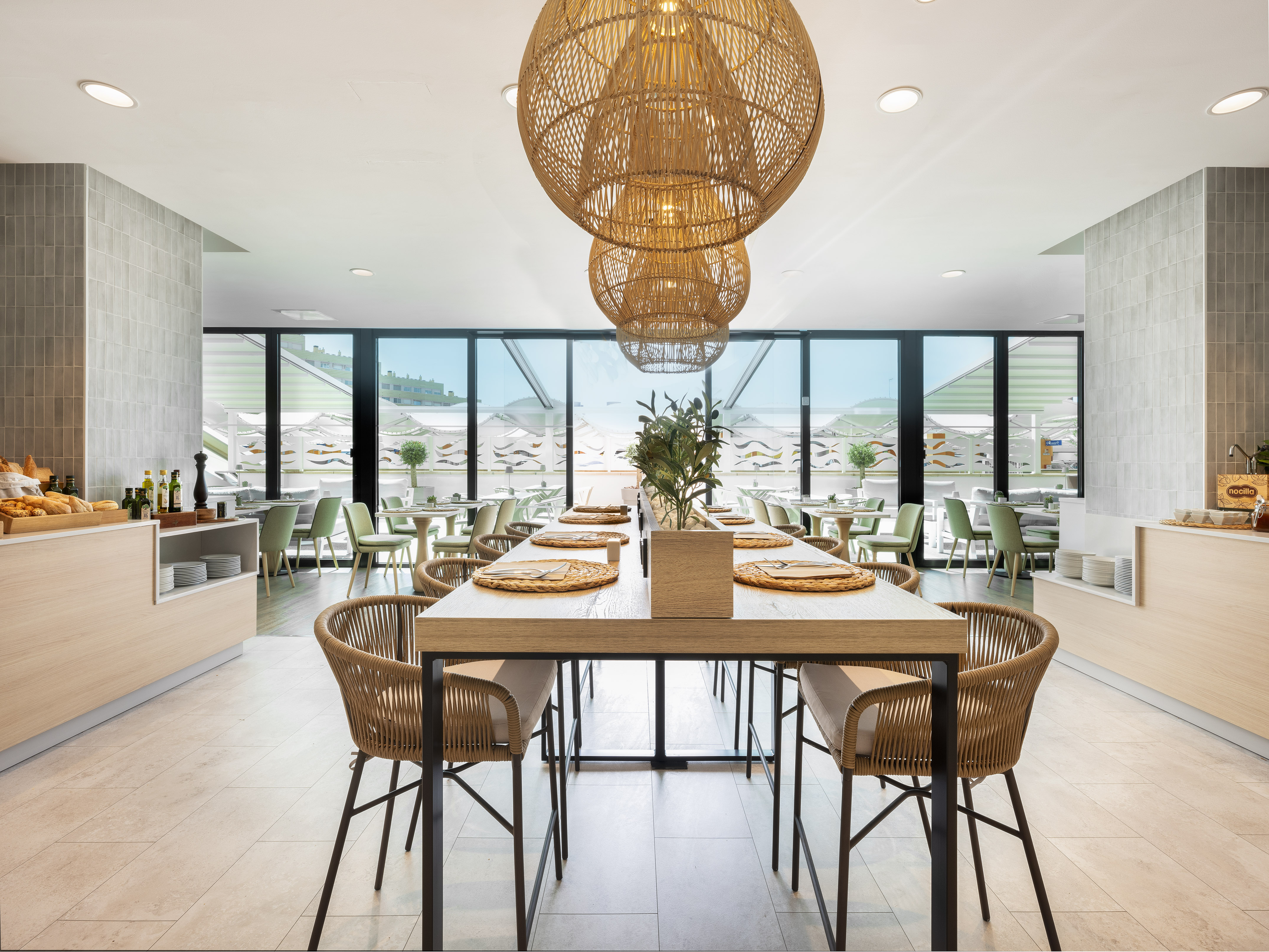 Comedor moderno de hotel con mesa larga, buffet y lámparas de mimbre.