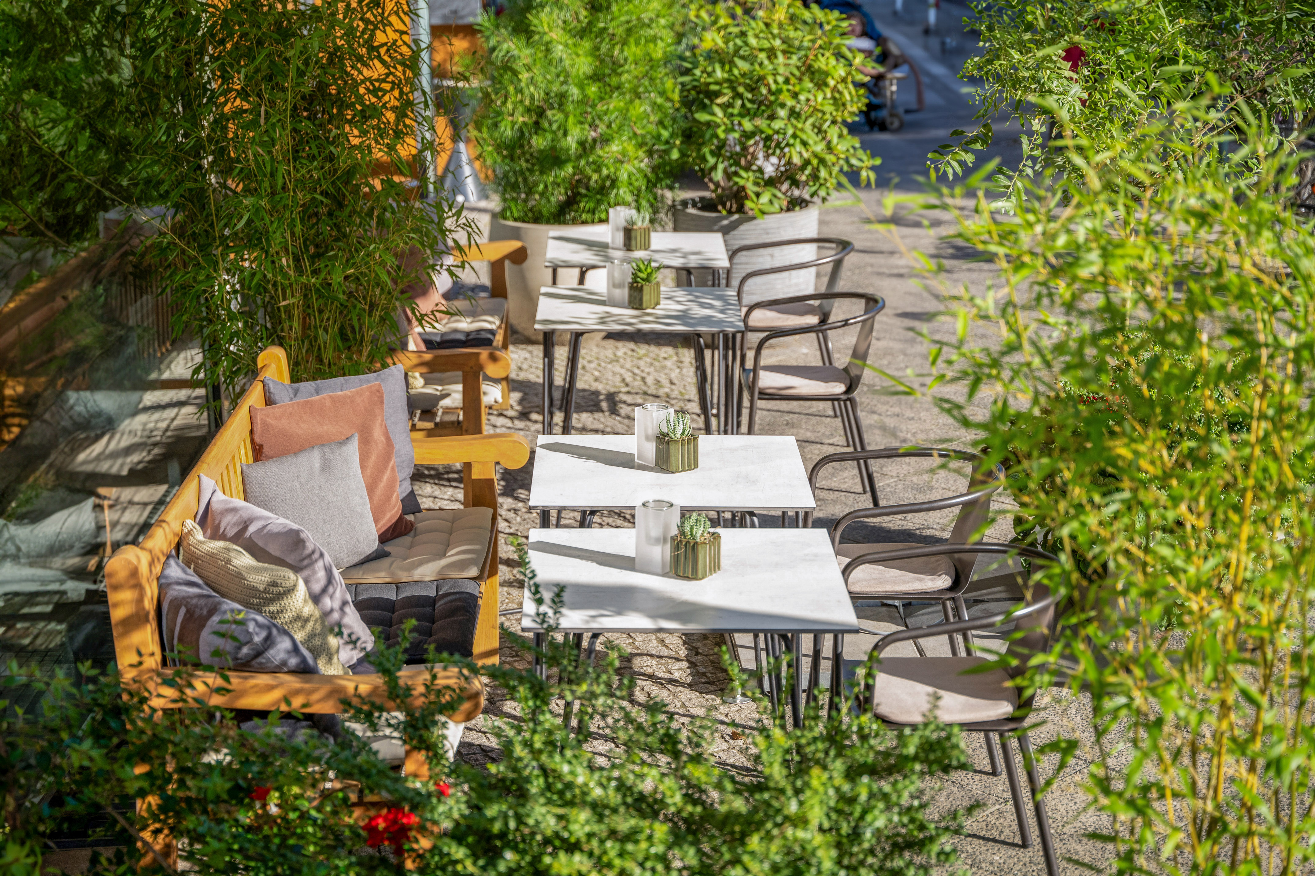 Sunny outdoor cafe patio with wooden benches, tables, chairs, and bamboo.
