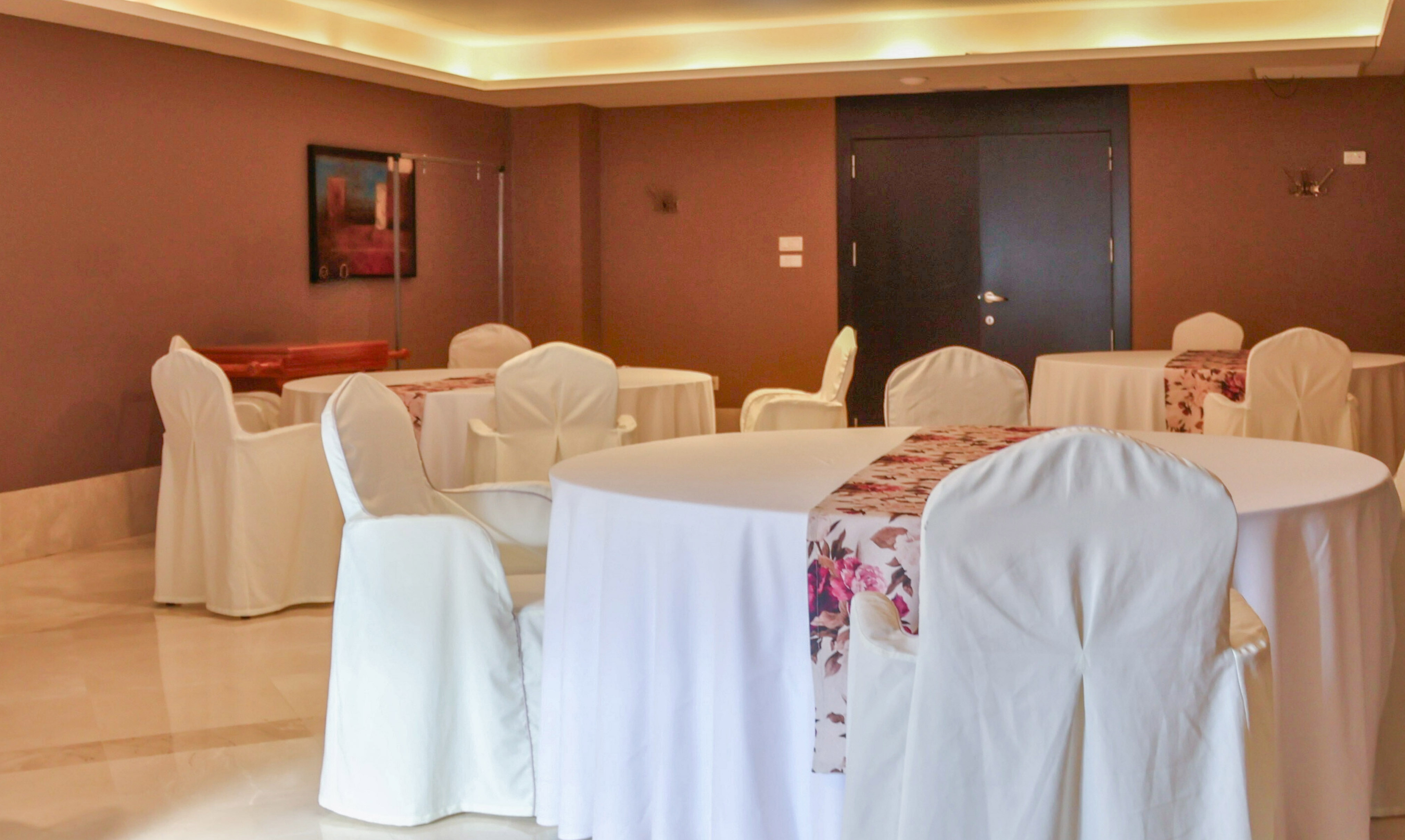 Empty banquet hall with white tables, covered chairs, and floral runners.