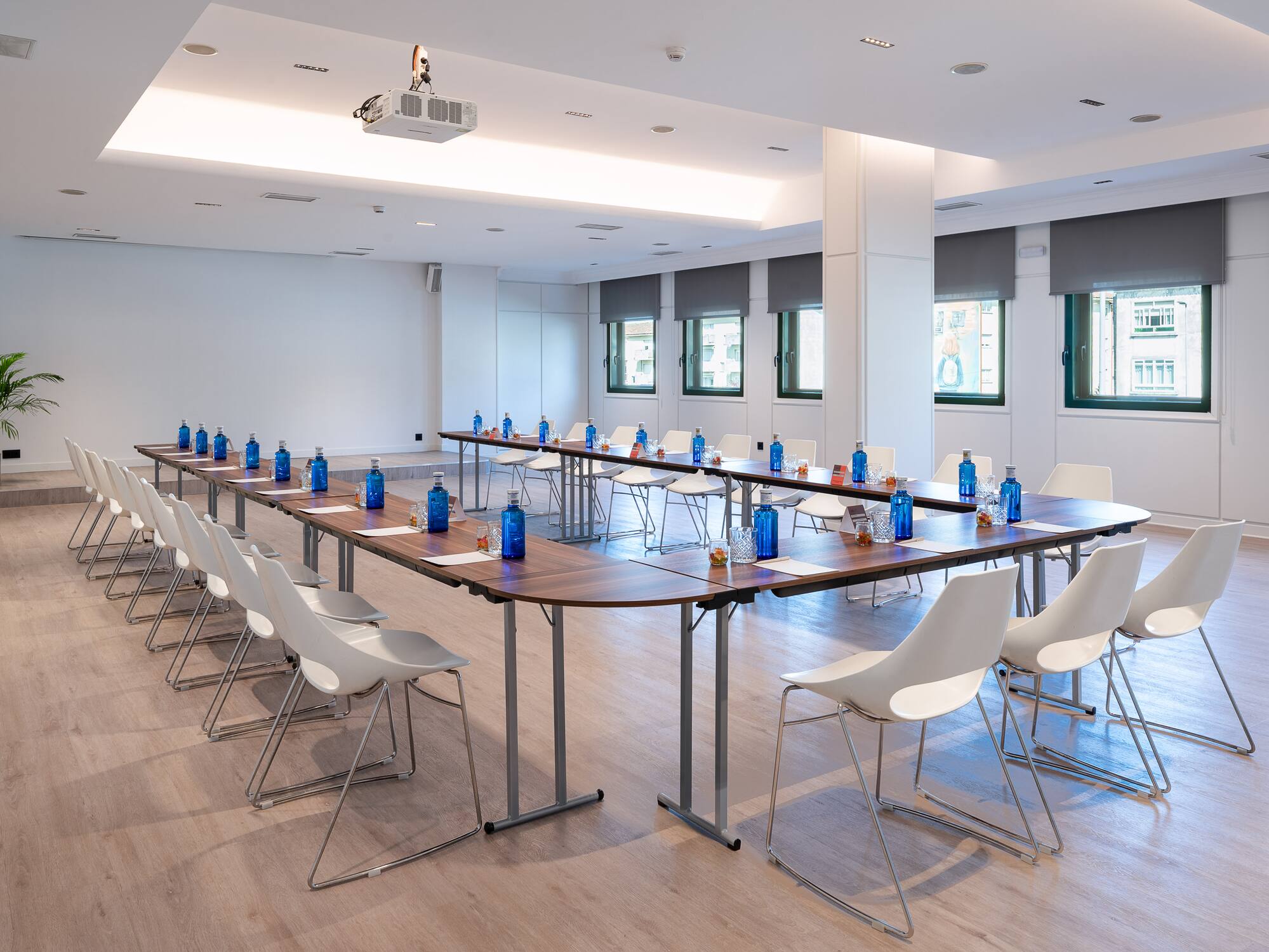 Contemporary conference room with U-shaped table, white chairs, projector, windows.