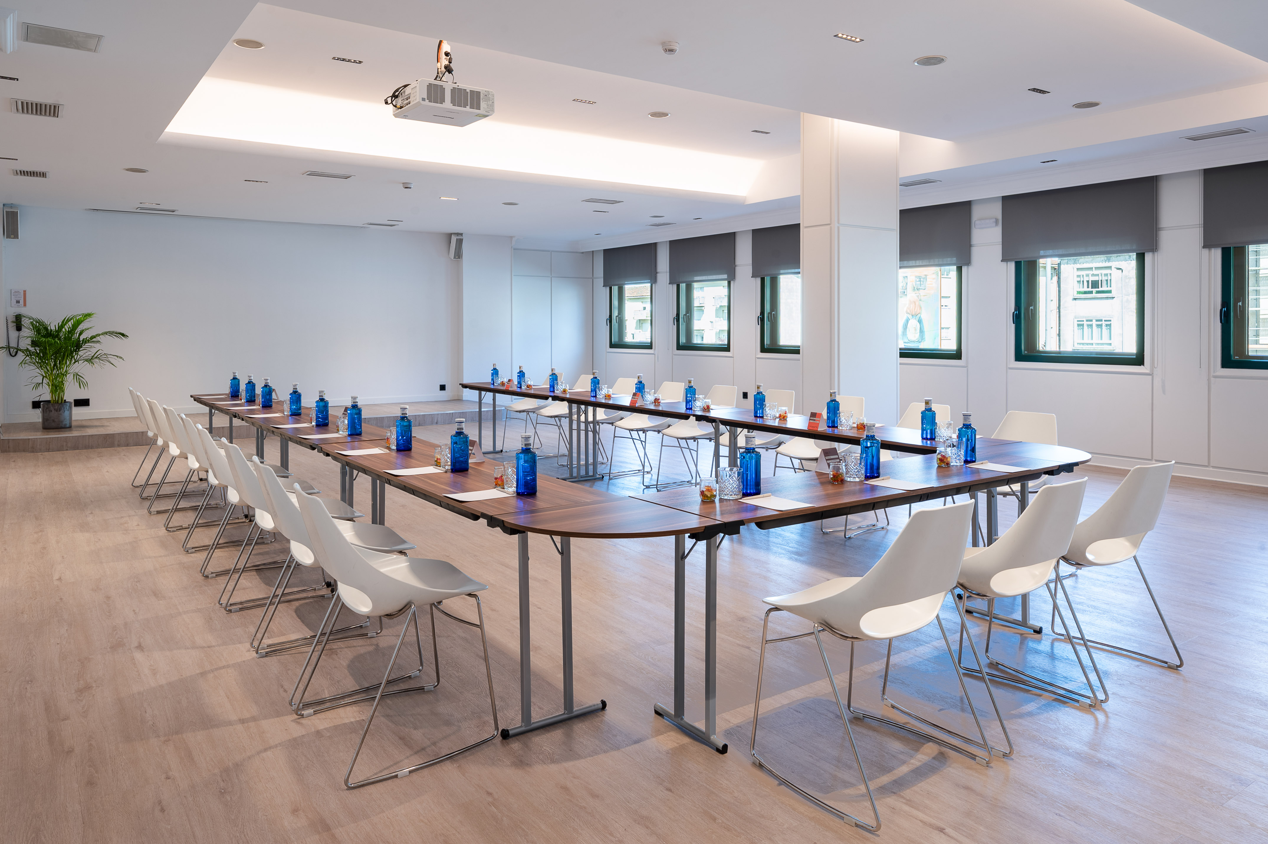 Moderna sala de reuniones en U con proyector, sillas blancas y botellas de agua.