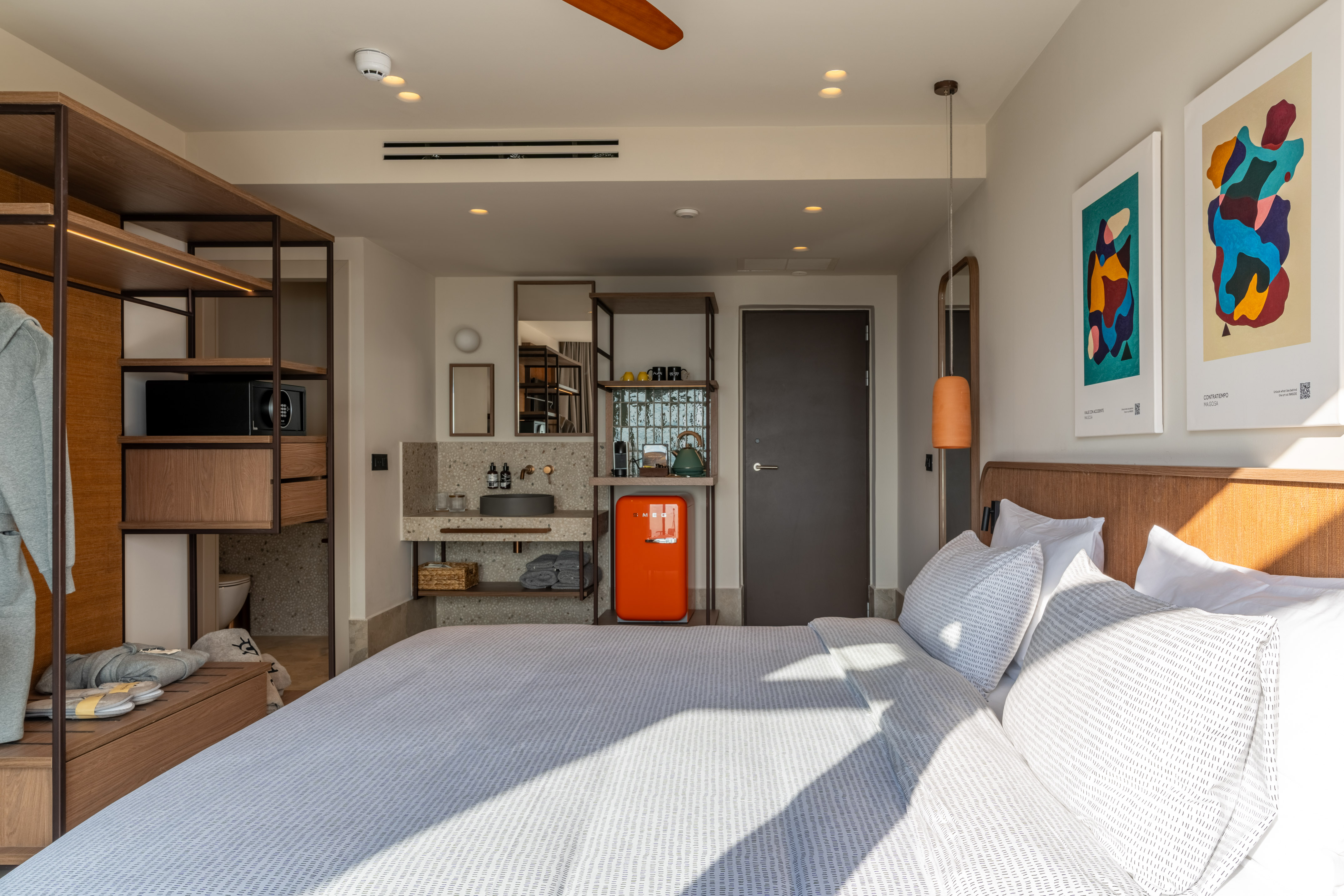 Stylish modern hotel room with bed, integrated storage, and orange SMEG fridge.