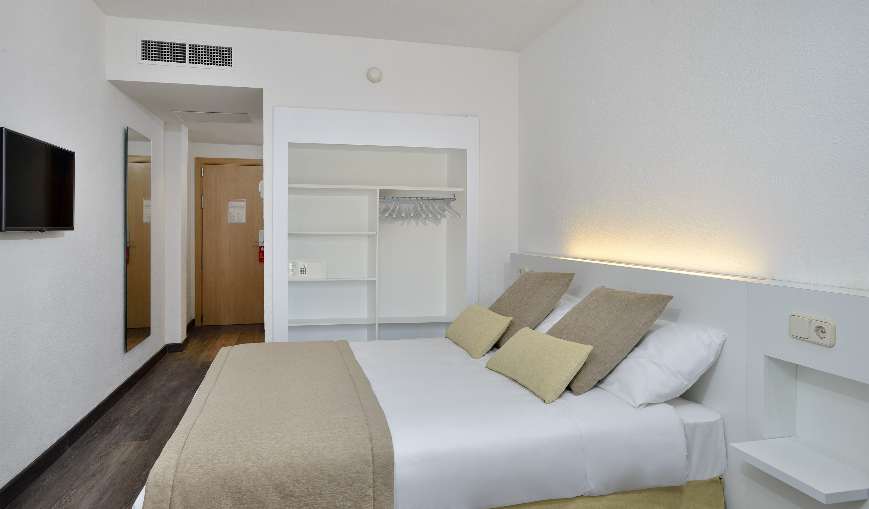 Modern hotel bedroom with white bed, built-in wardrobe, wall TV, and wood floor.