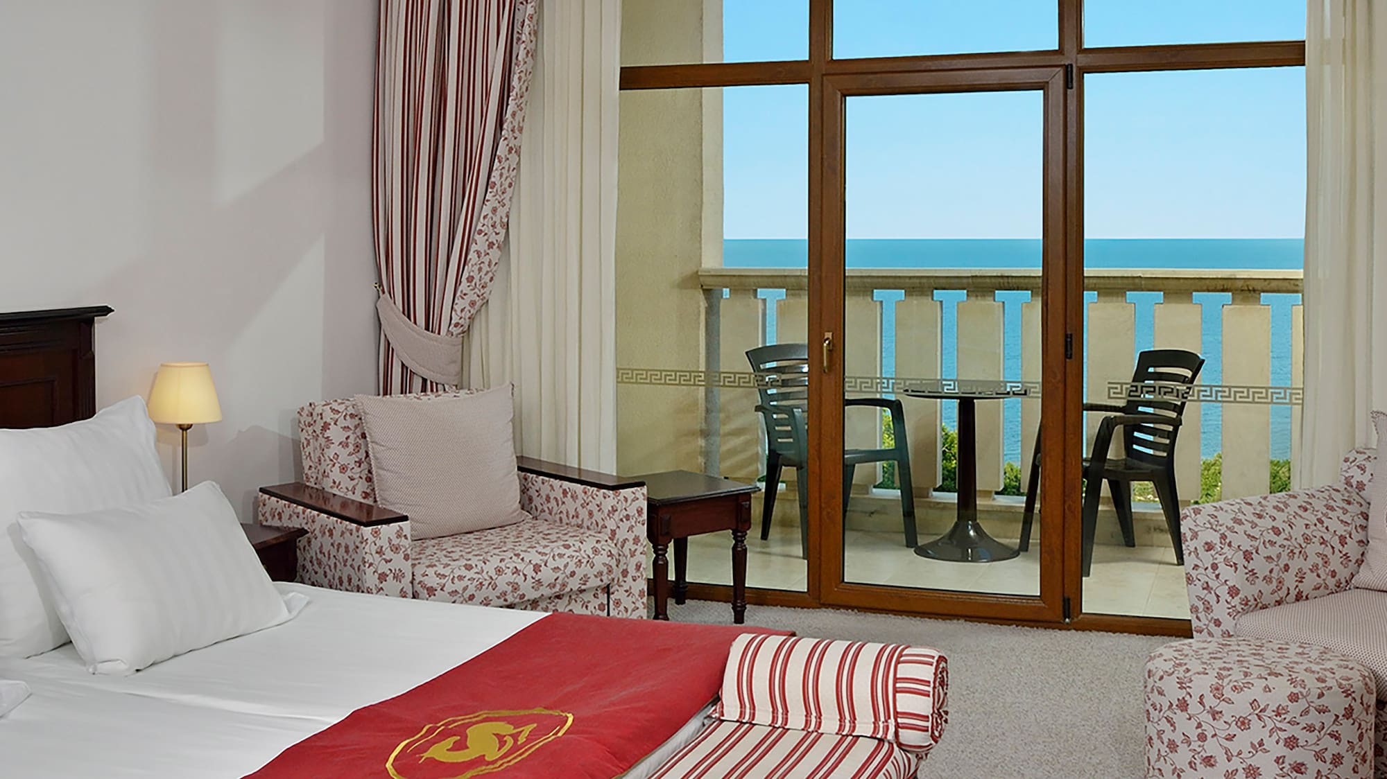 a room with a bed and chairs and a balcony overlooking the ocean