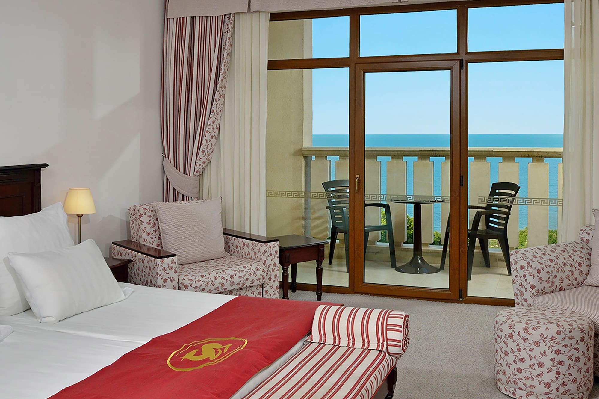 a room with a bed and chairs and a balcony overlooking the ocean