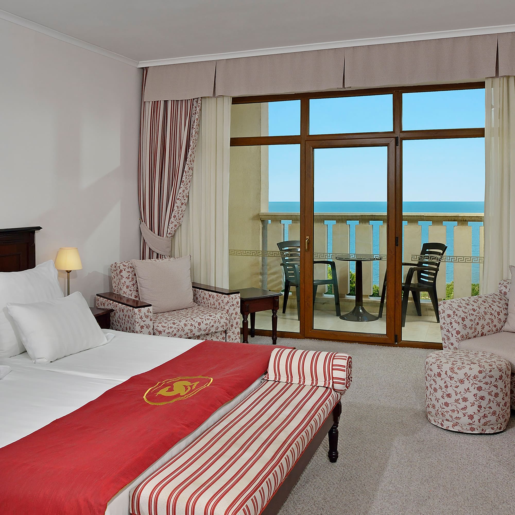 a room with a bed and chairs and a balcony overlooking the ocean