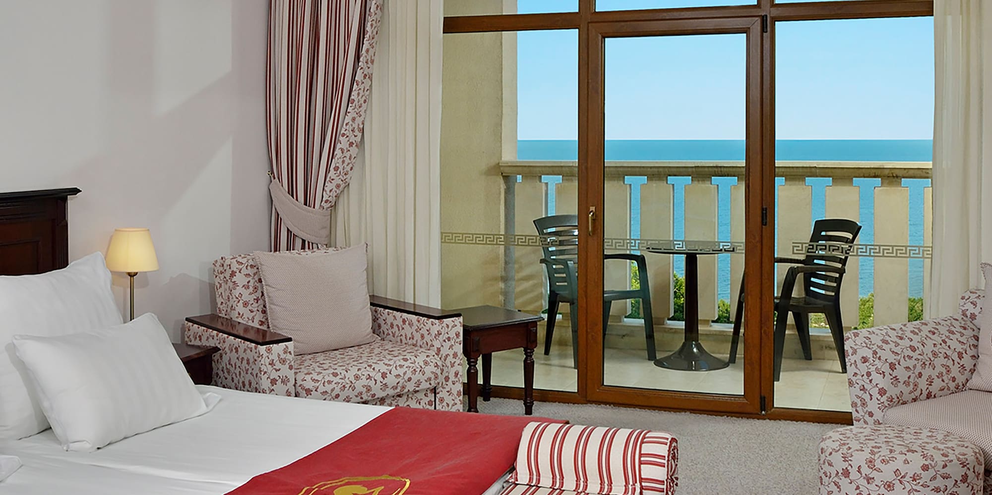 a room with a bed and chairs and a balcony overlooking the ocean