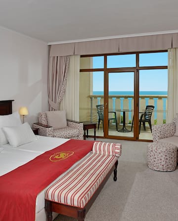 a room with a bed and chairs and a balcony overlooking the ocean