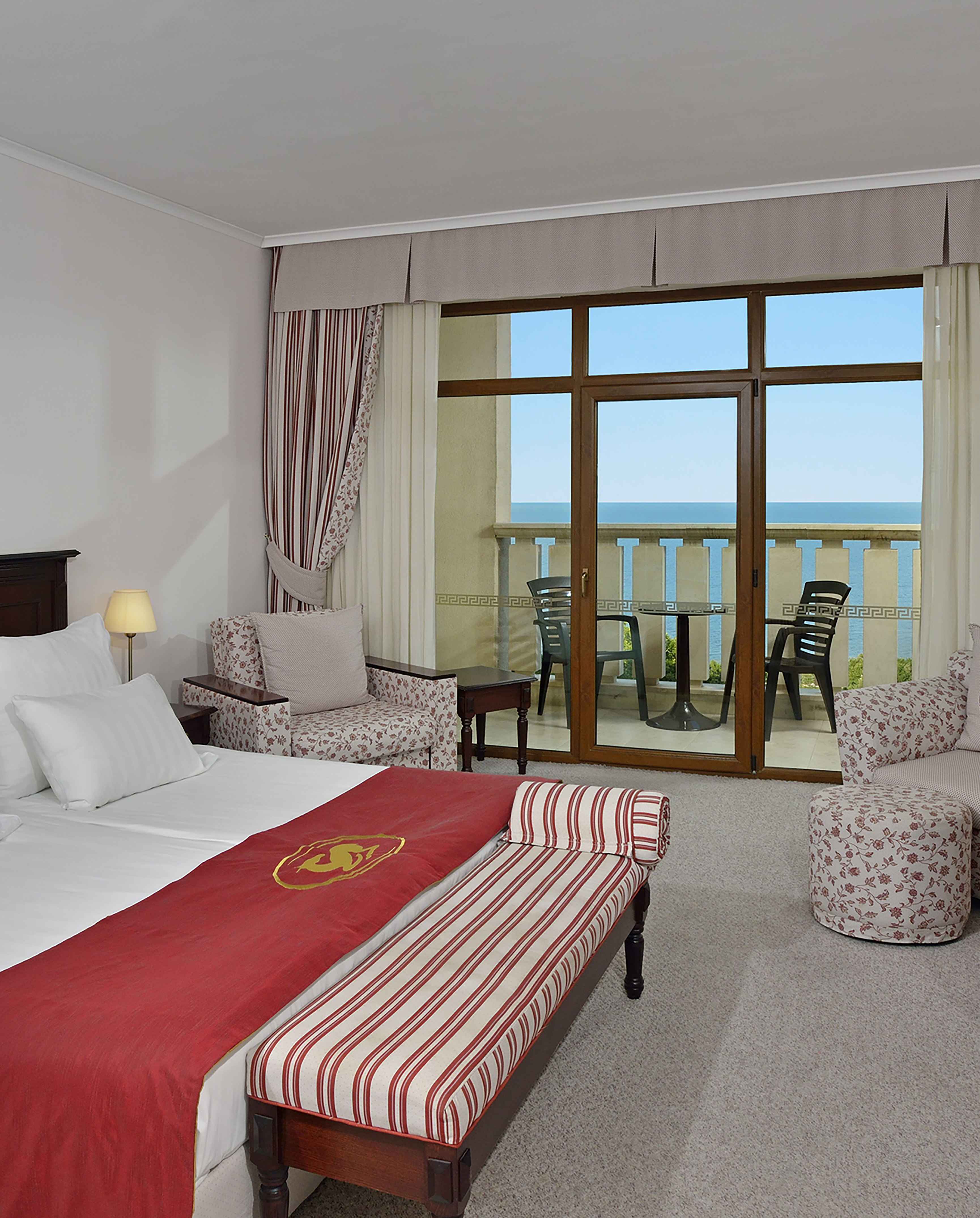 a room with a bed and chairs and a balcony overlooking the ocean