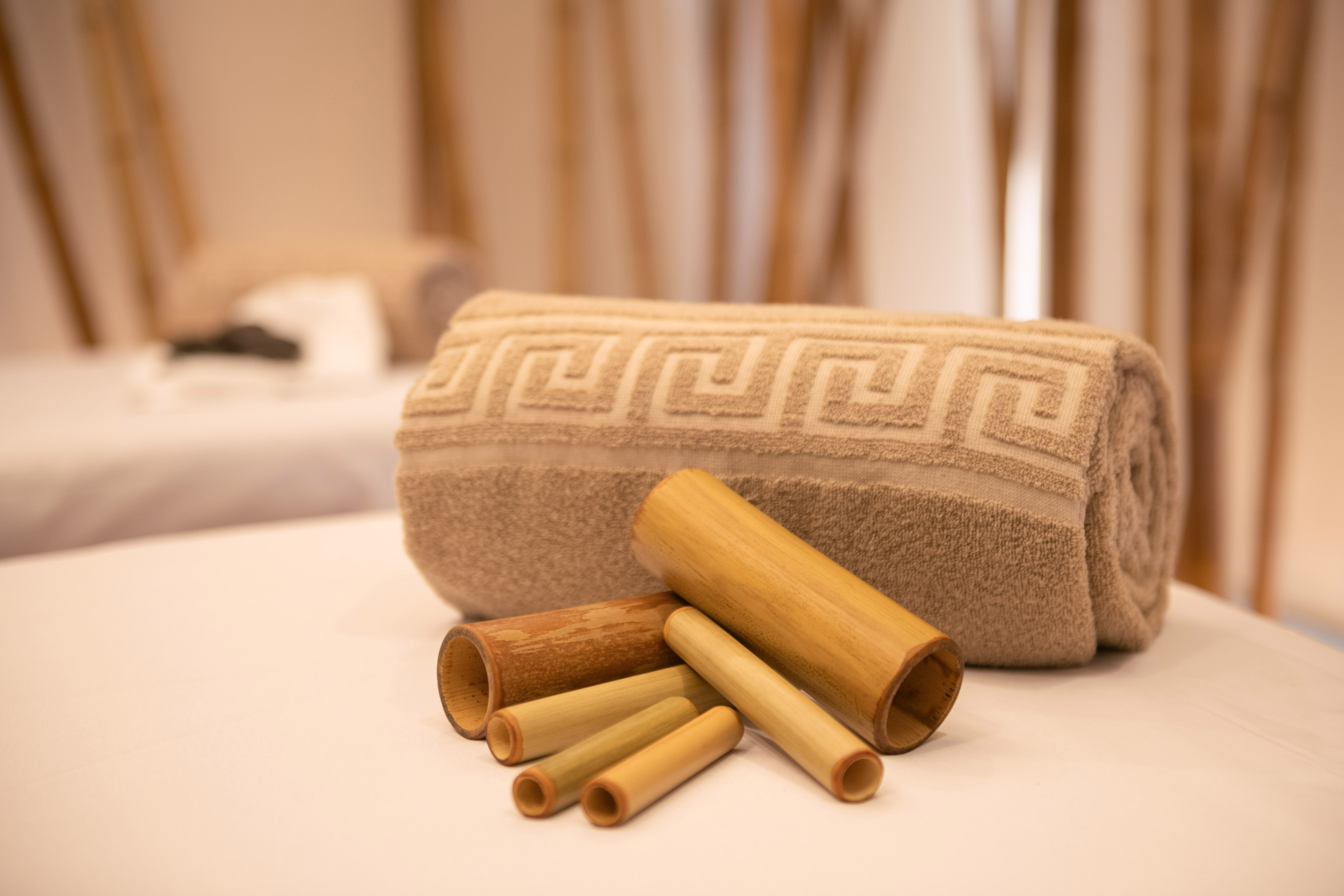 Rolled patterned spa towel and bamboo massage tools on a treatment bed.