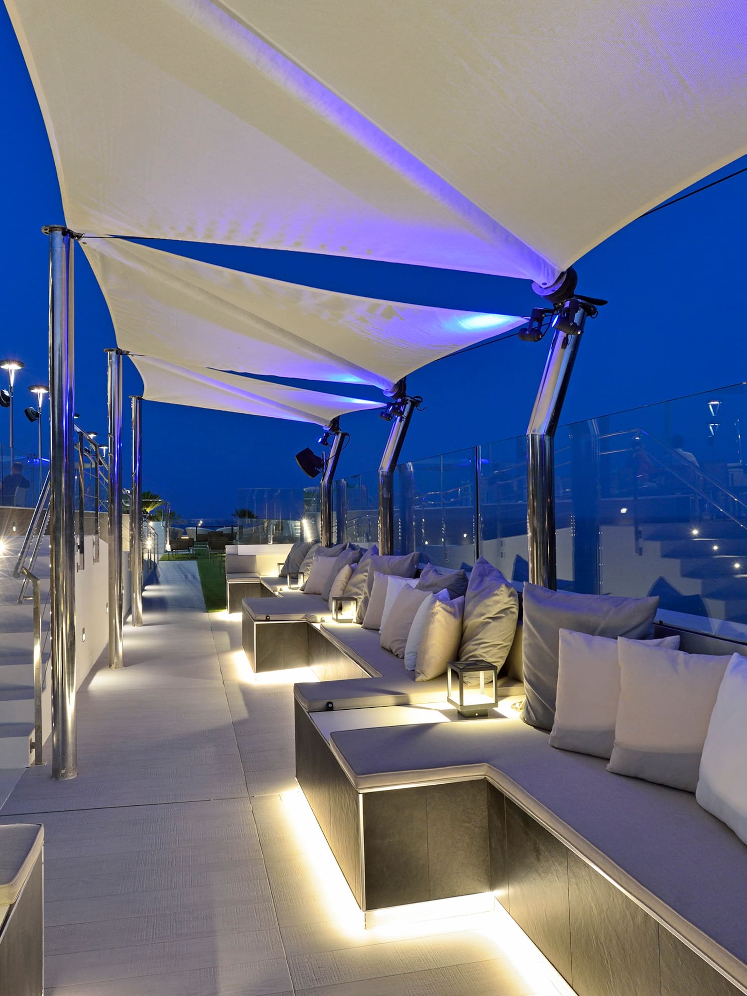 Modern rooftop lounge with illuminated seating, steps, and canopies at night.