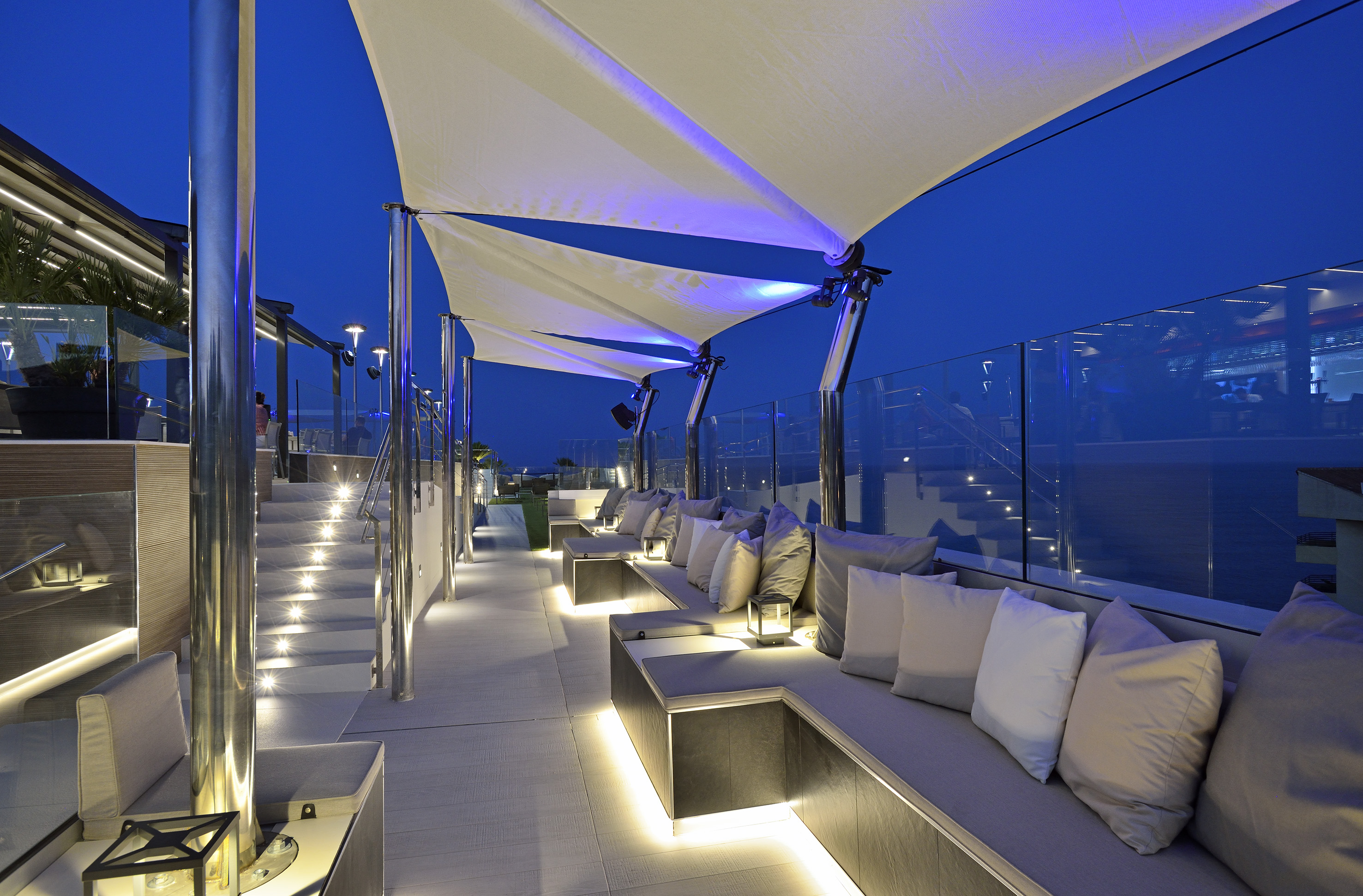 Modern rooftop lounge with illuminated seating, steps, and canopies at night.