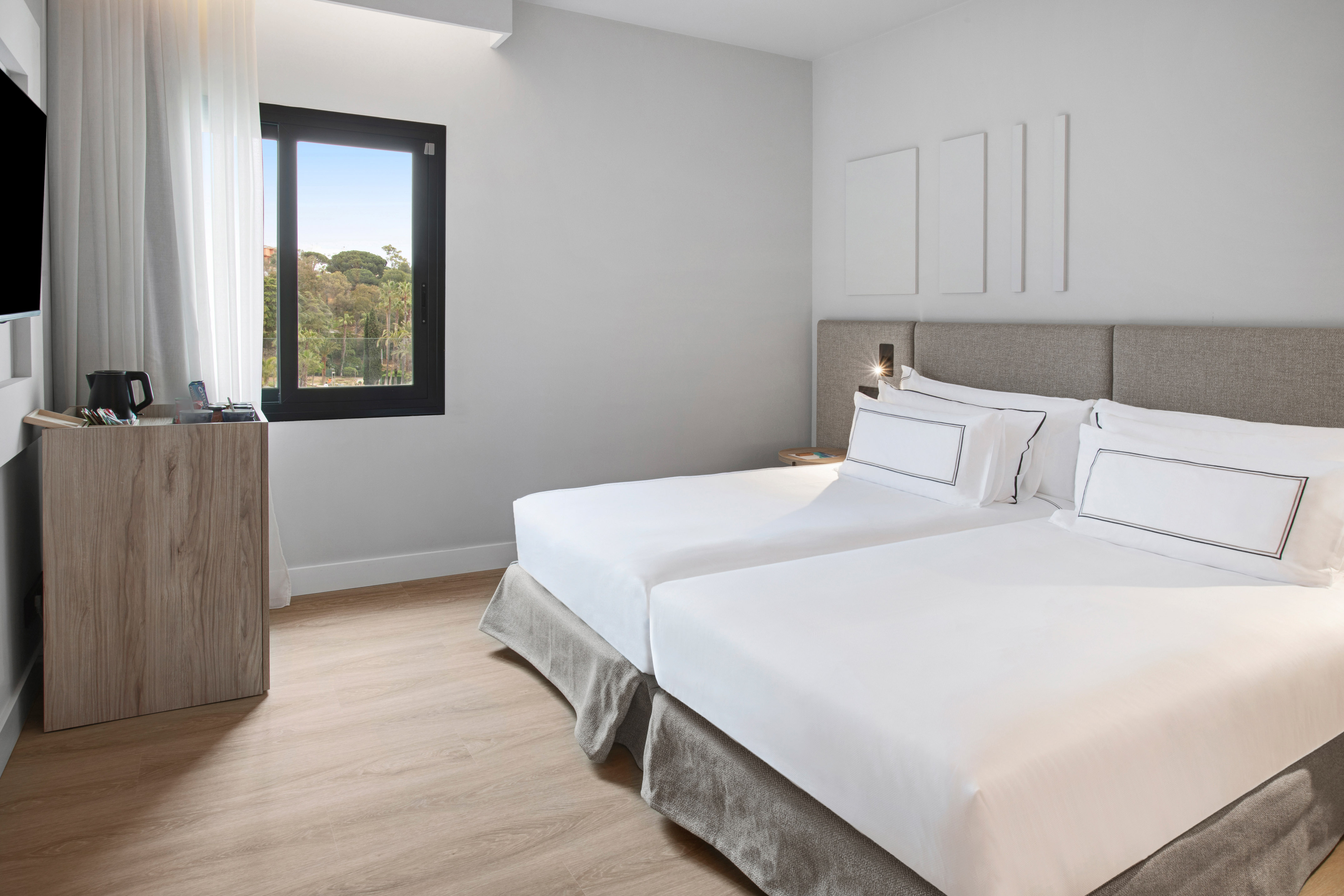 Bright modern hotel room with twin beds, natural light, and green forest view.