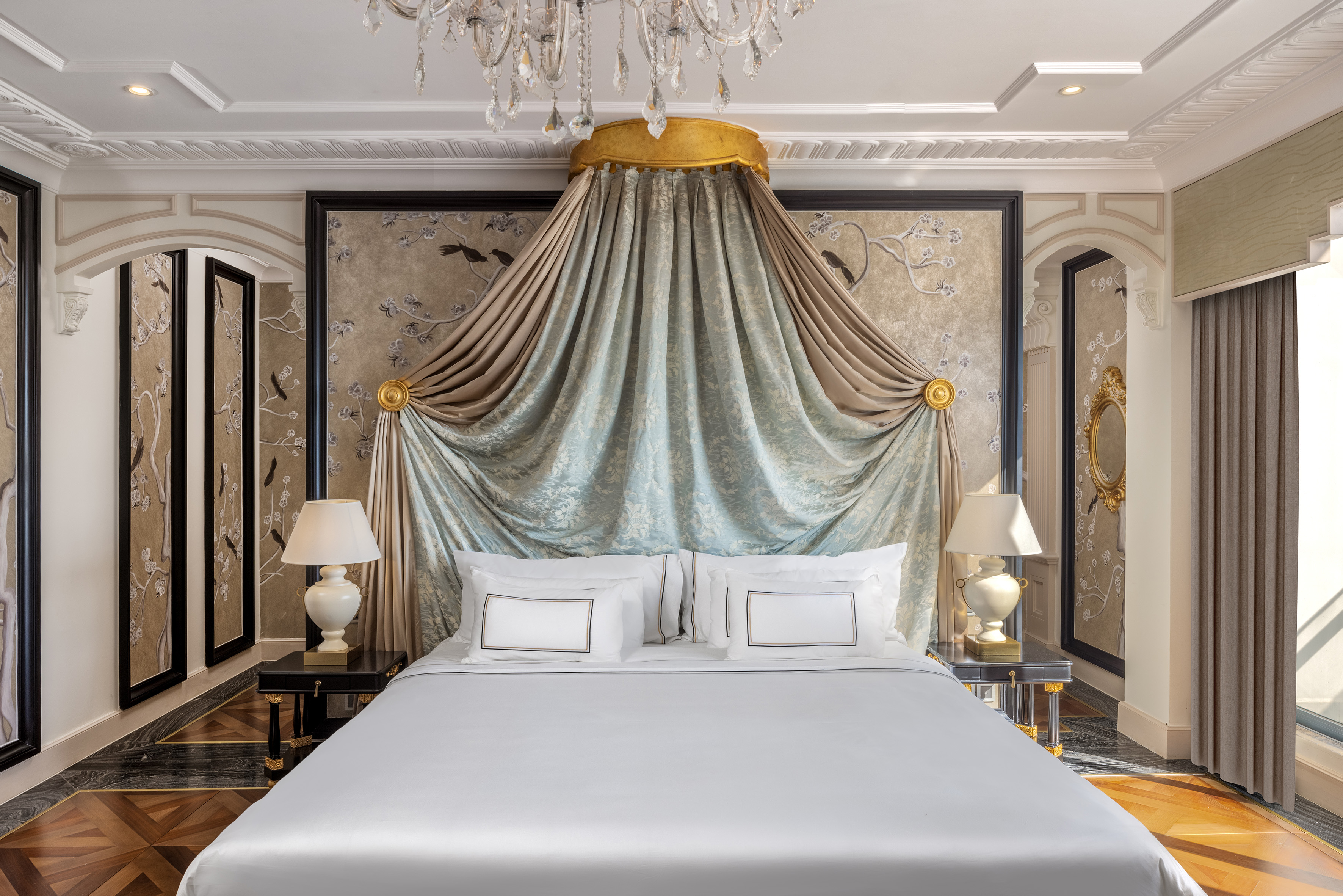 Elegant canopy bed in a luxurious bedroom with ornate wallpaper and chandelier.