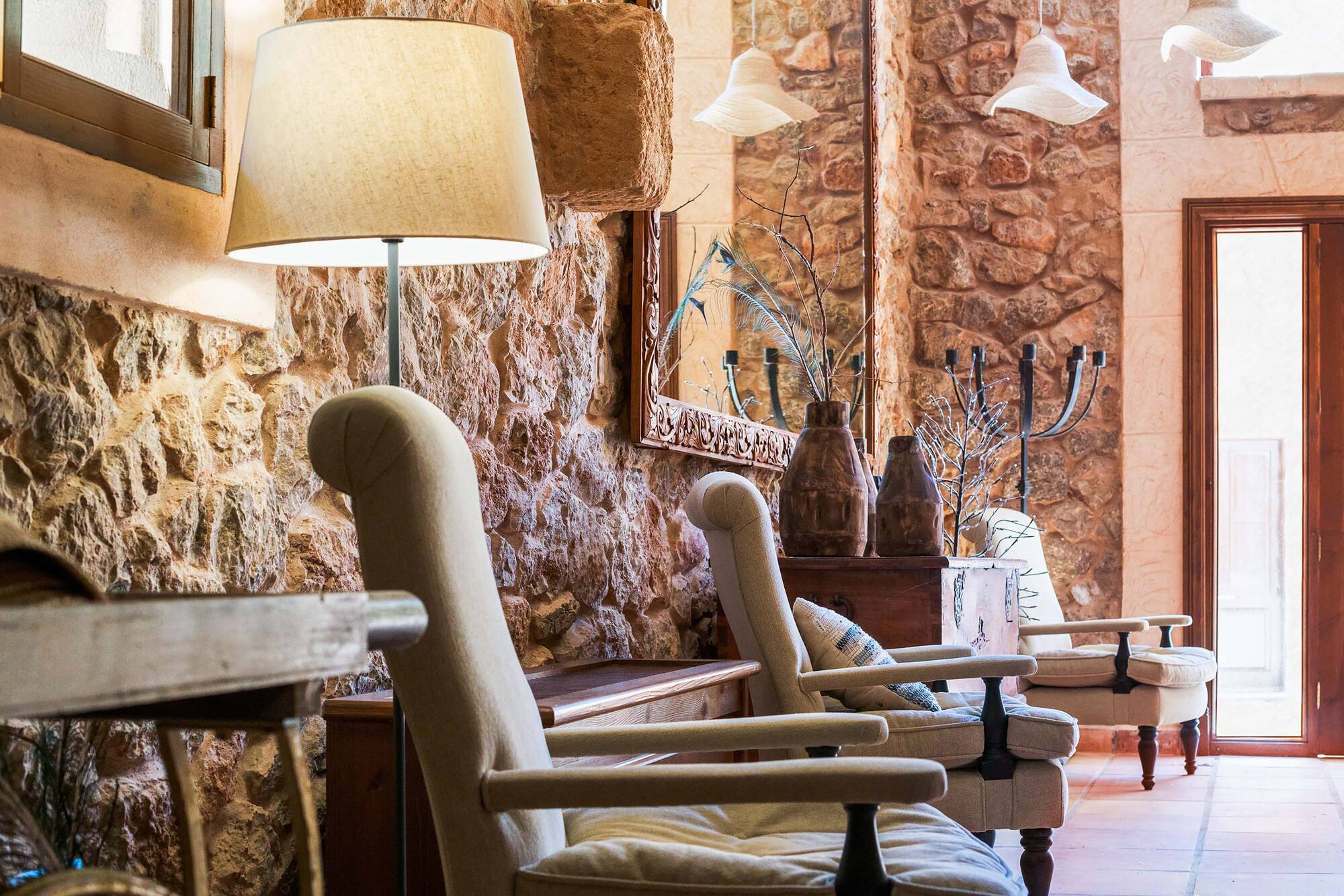 Rustic living room with stone walls, cozy armchairs, floor lamp, and mirror.