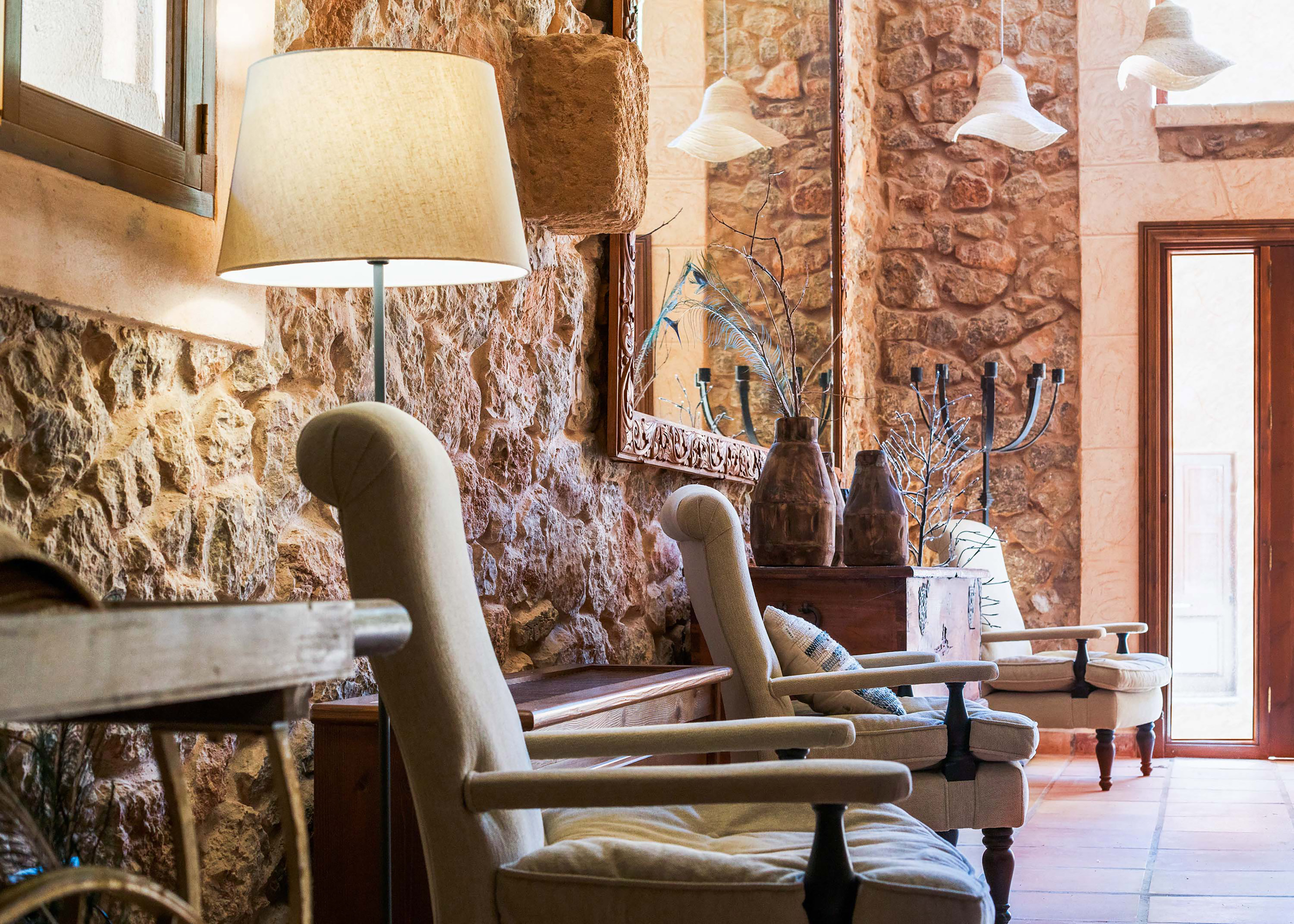 Rustic living room with stone walls, cozy armchairs, floor lamp, and mirror.