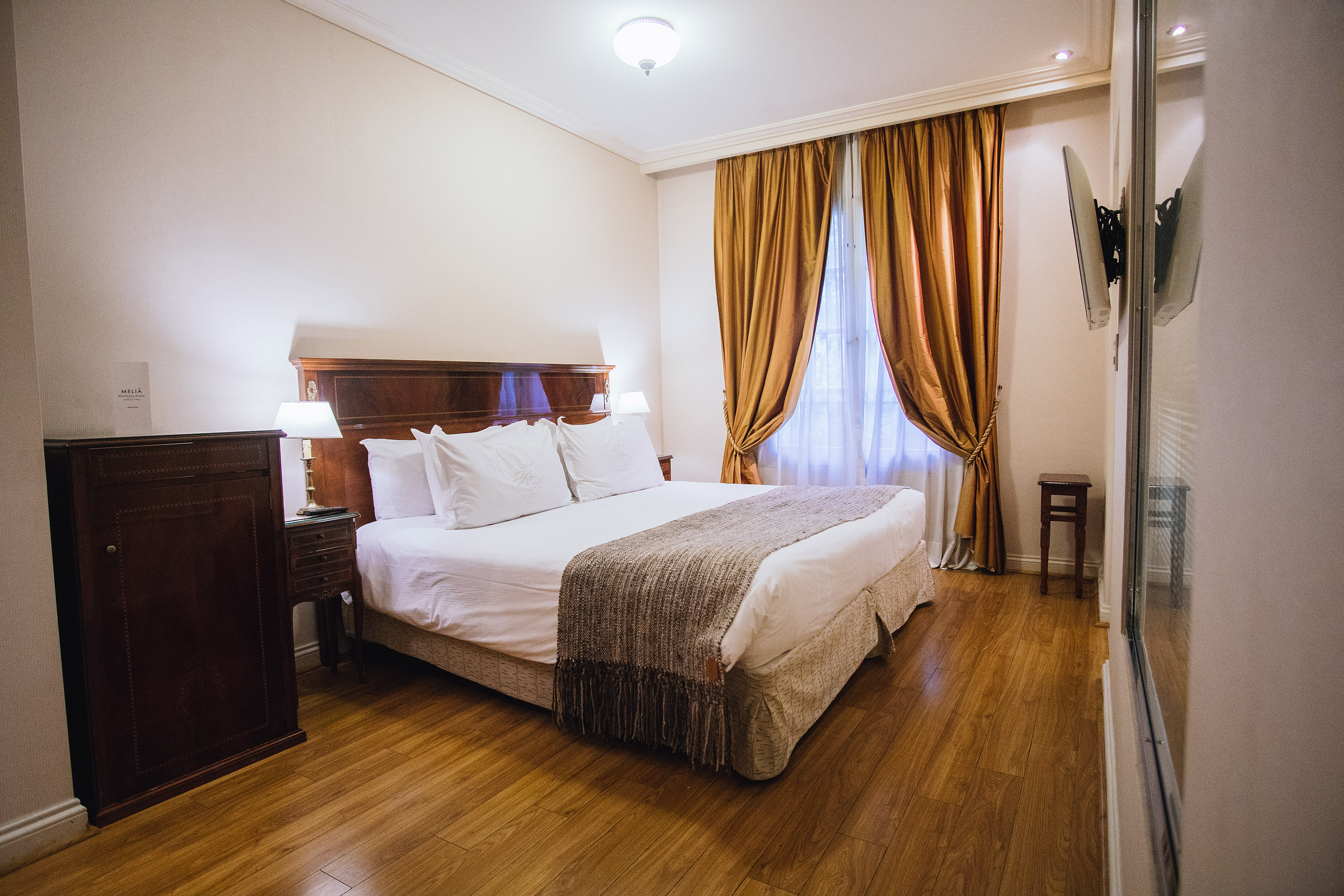 Comfortable hotel bedroom with king bed, wood floor, and golden drapes.