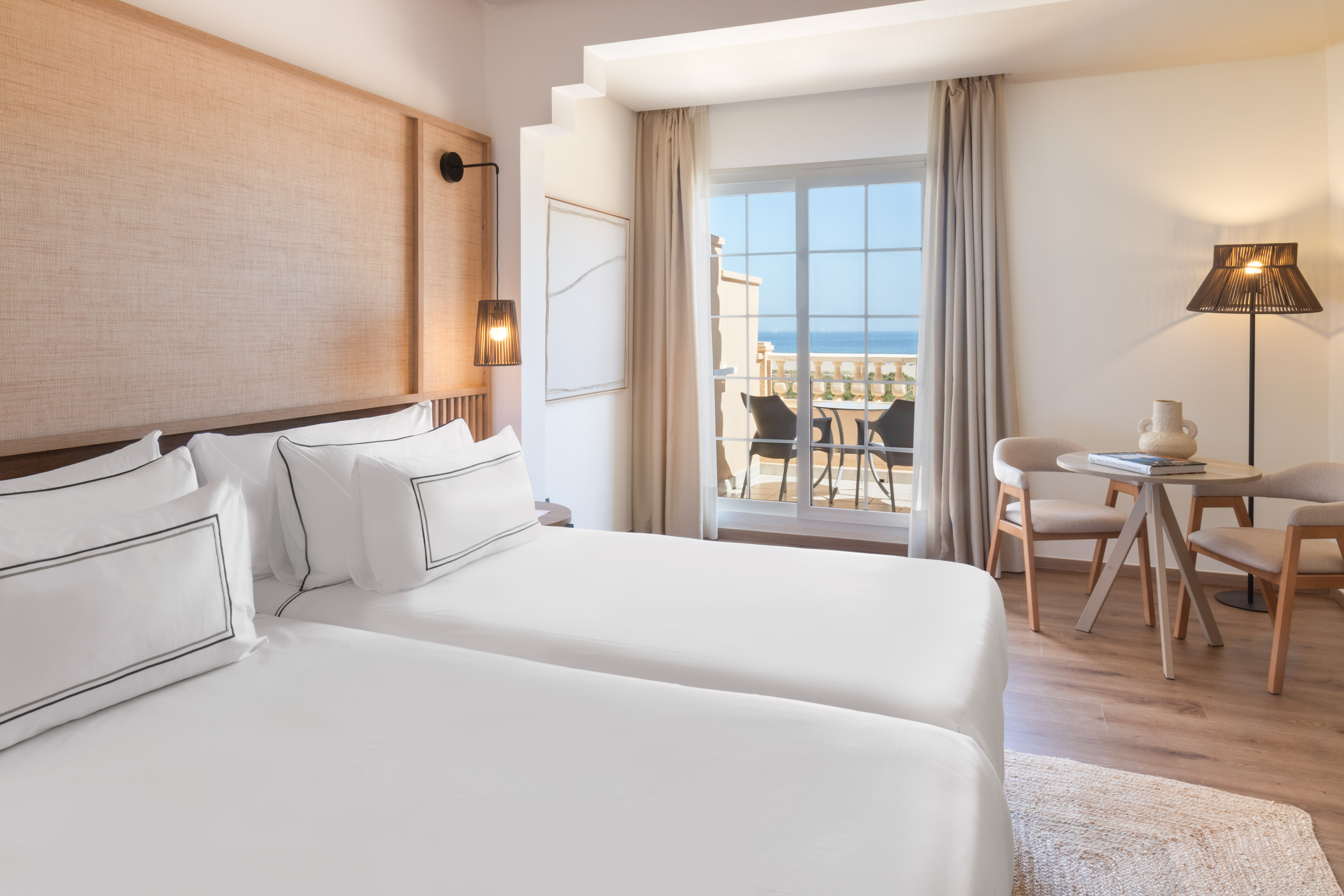 Hotel room with twin beds, balcony, and panoramic ocean view.