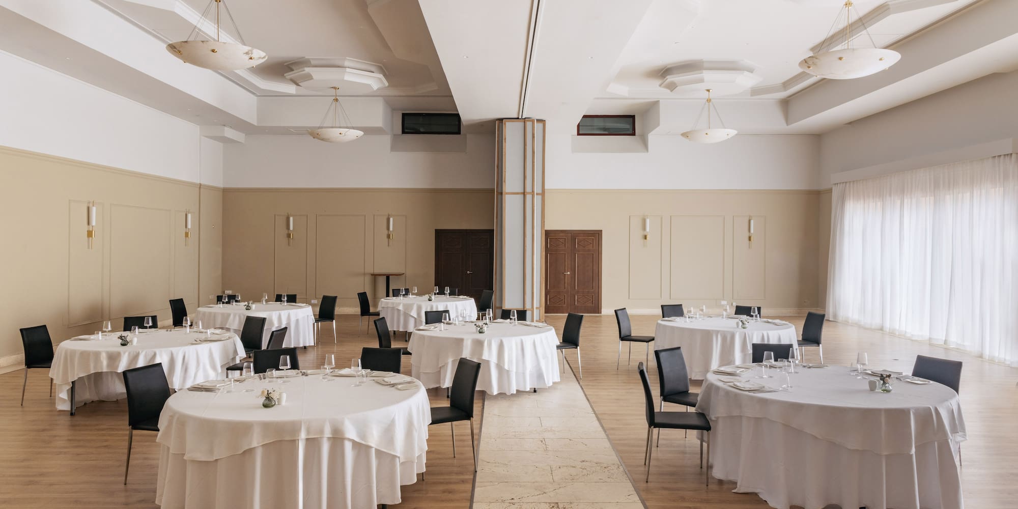Spacious banquet hall with round dining tables, white linens, black chairs.