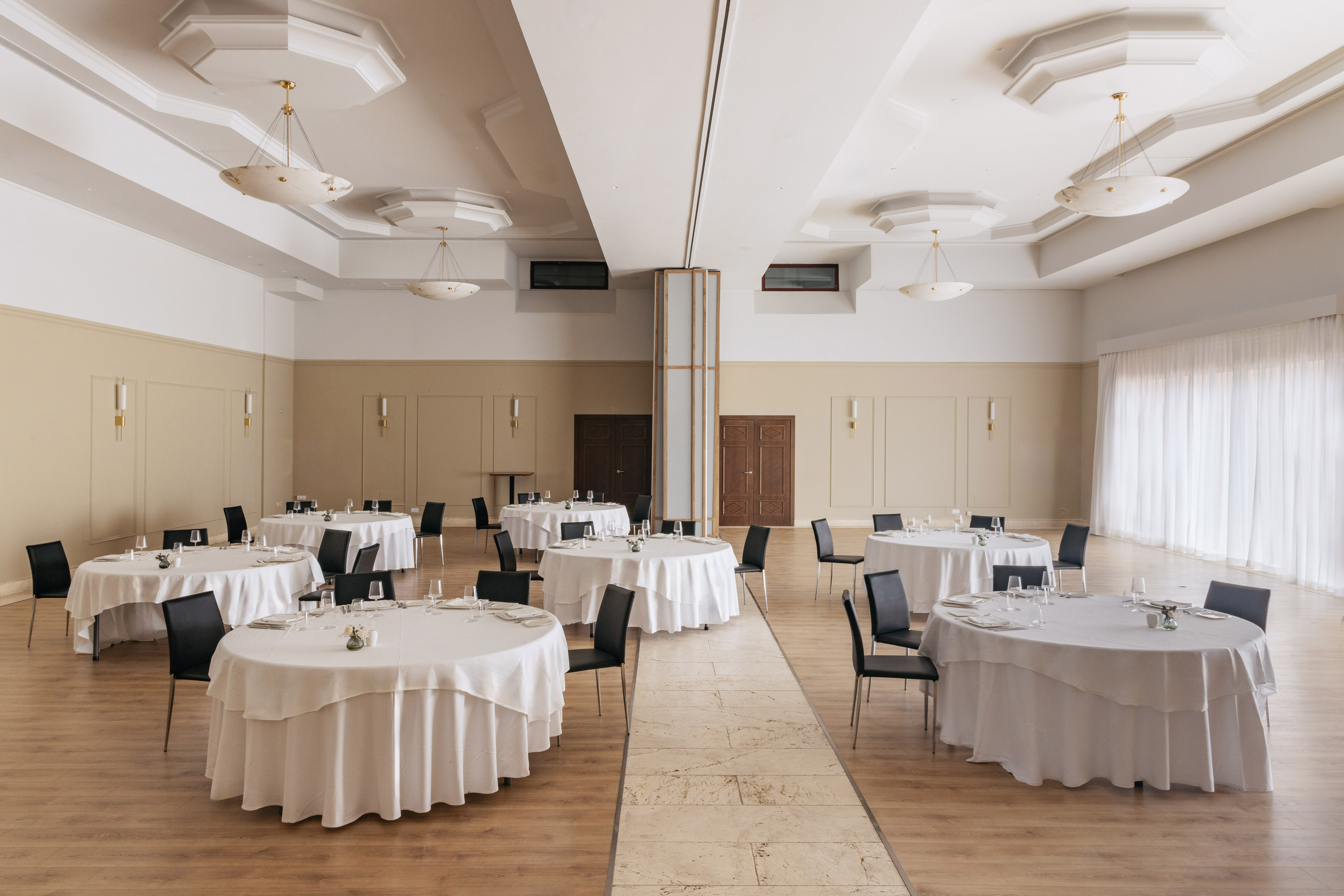Spacious banquet hall with round dining tables, white linens, black chairs.