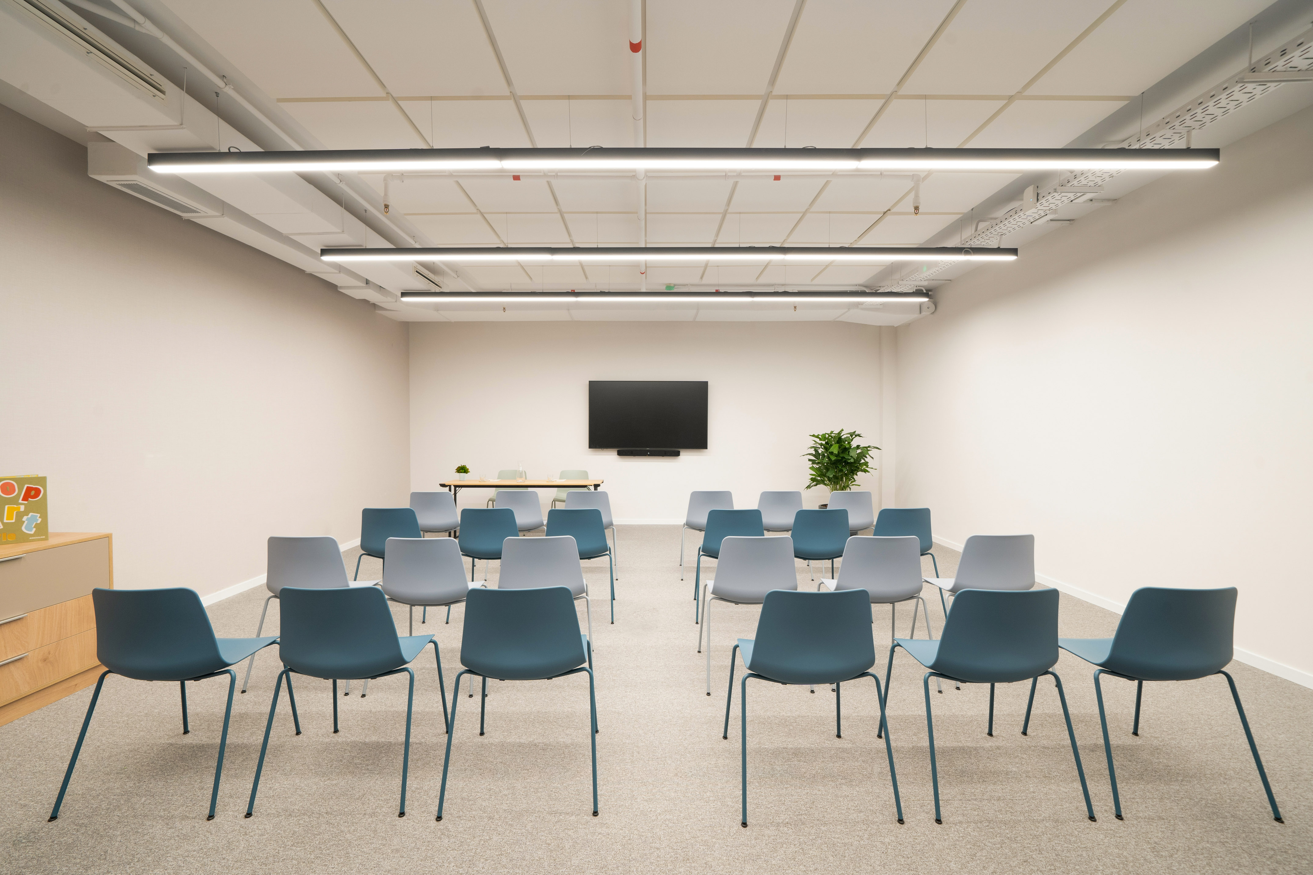 Modern conference room with rows of blue and gray chairs, large screen.