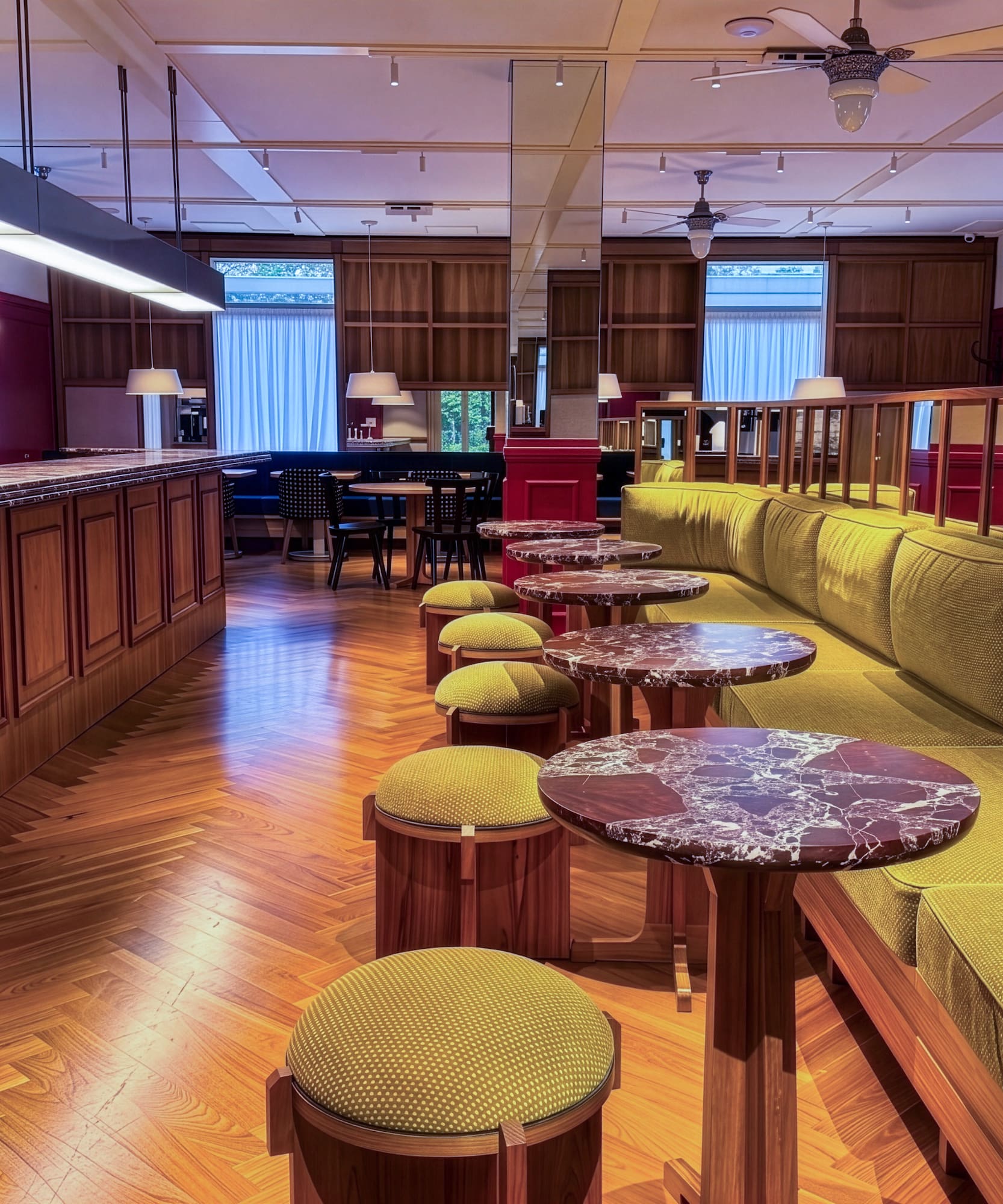 Elegant bar lounge with wood counter, green banquette, marble tables, herringbone floor.