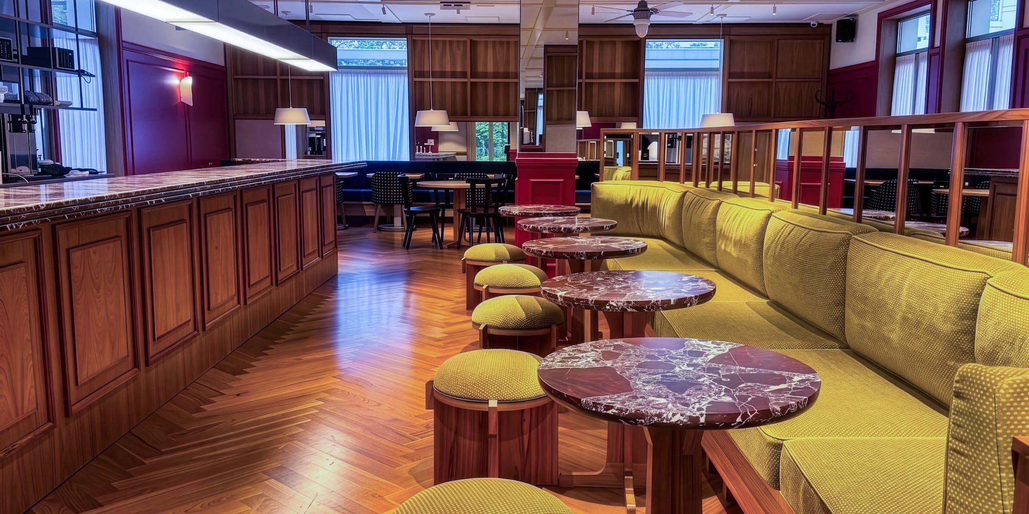 Elegant bar lounge with green banquette, marble tables, and wood herringbone floor.