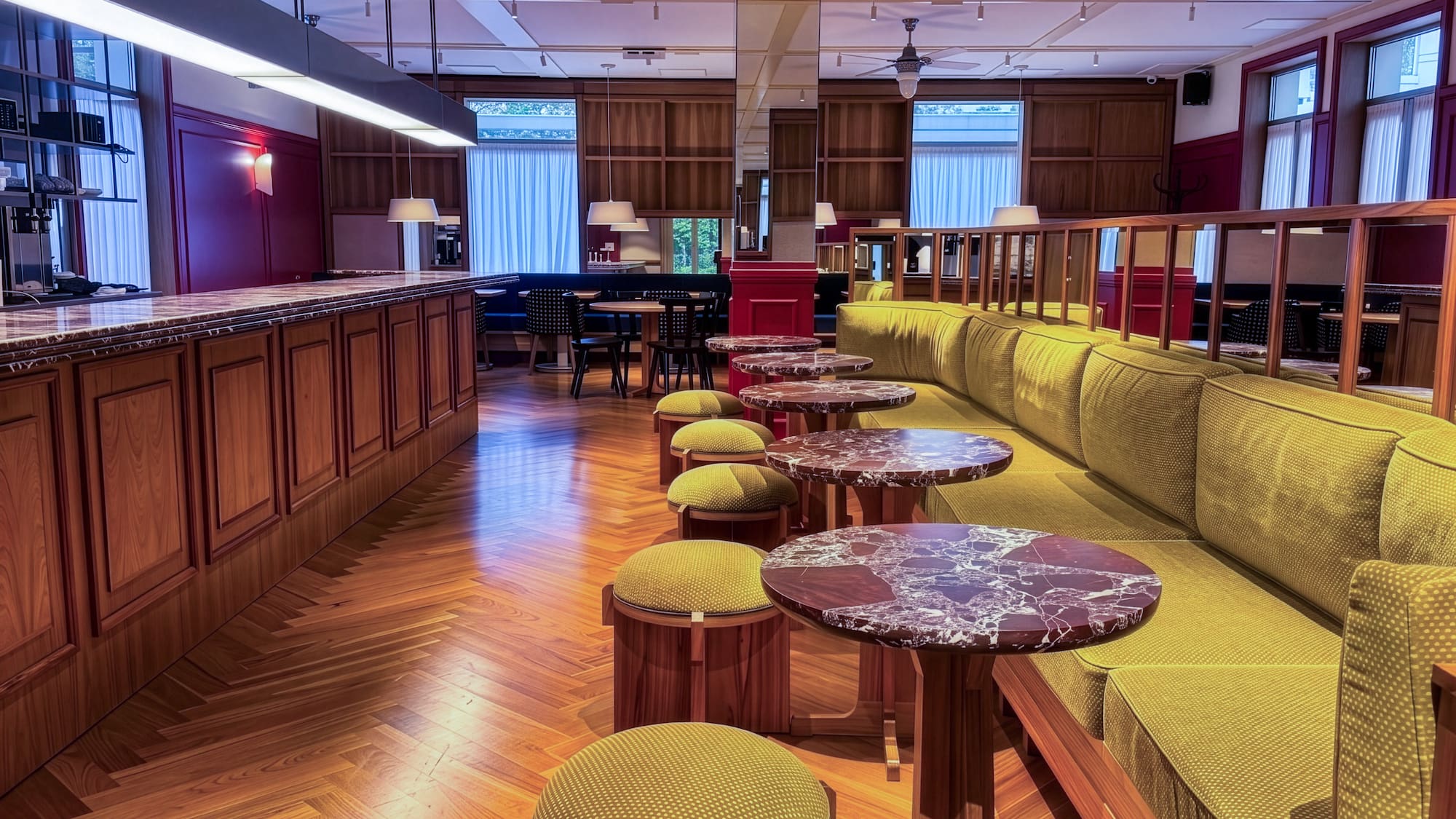 Green velvet banquet seating, marble tables, and wood bar in an elegant lounge.