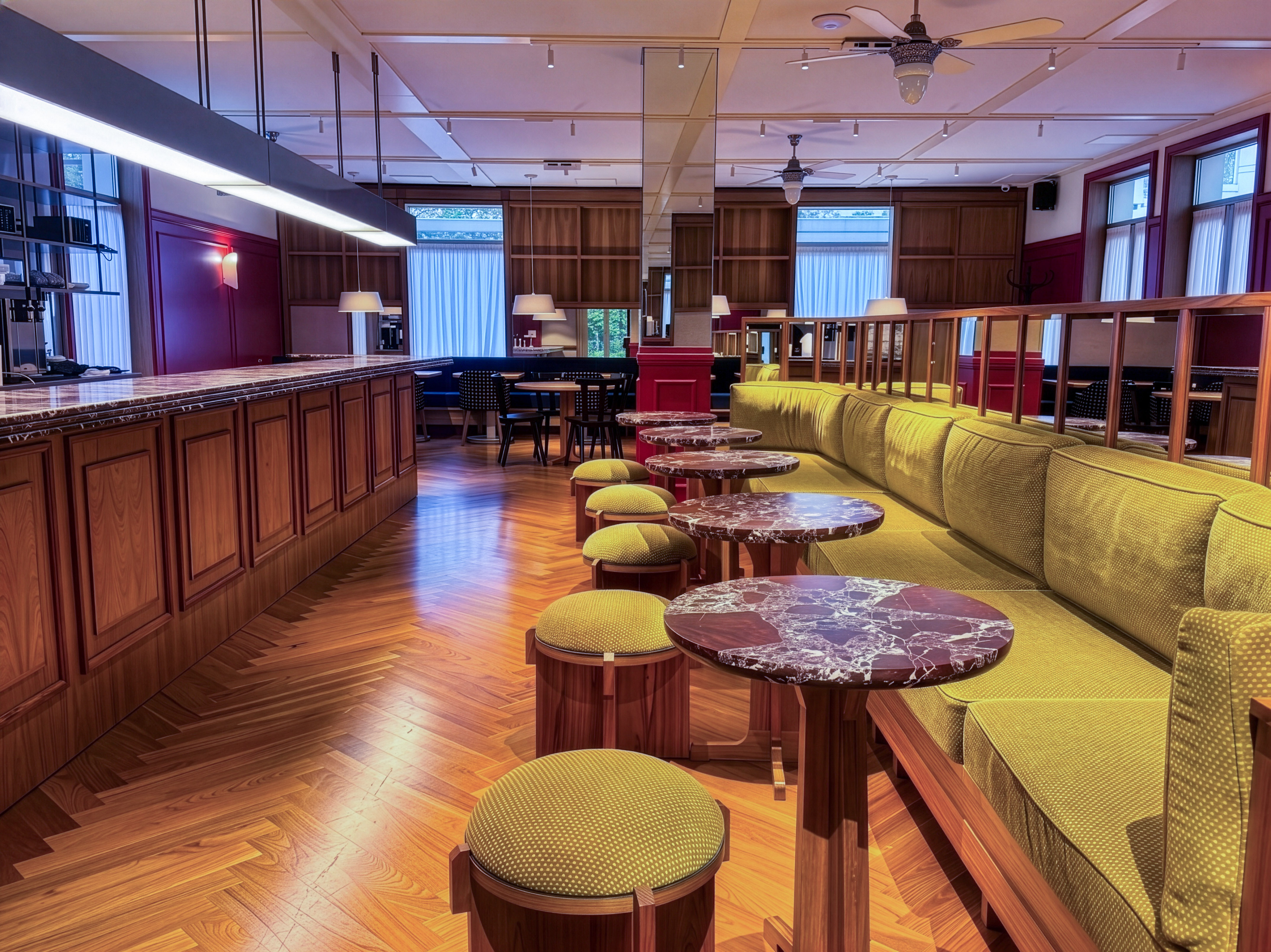 Green velvet banquet seating, marble tables, and wood bar in an elegant lounge.
