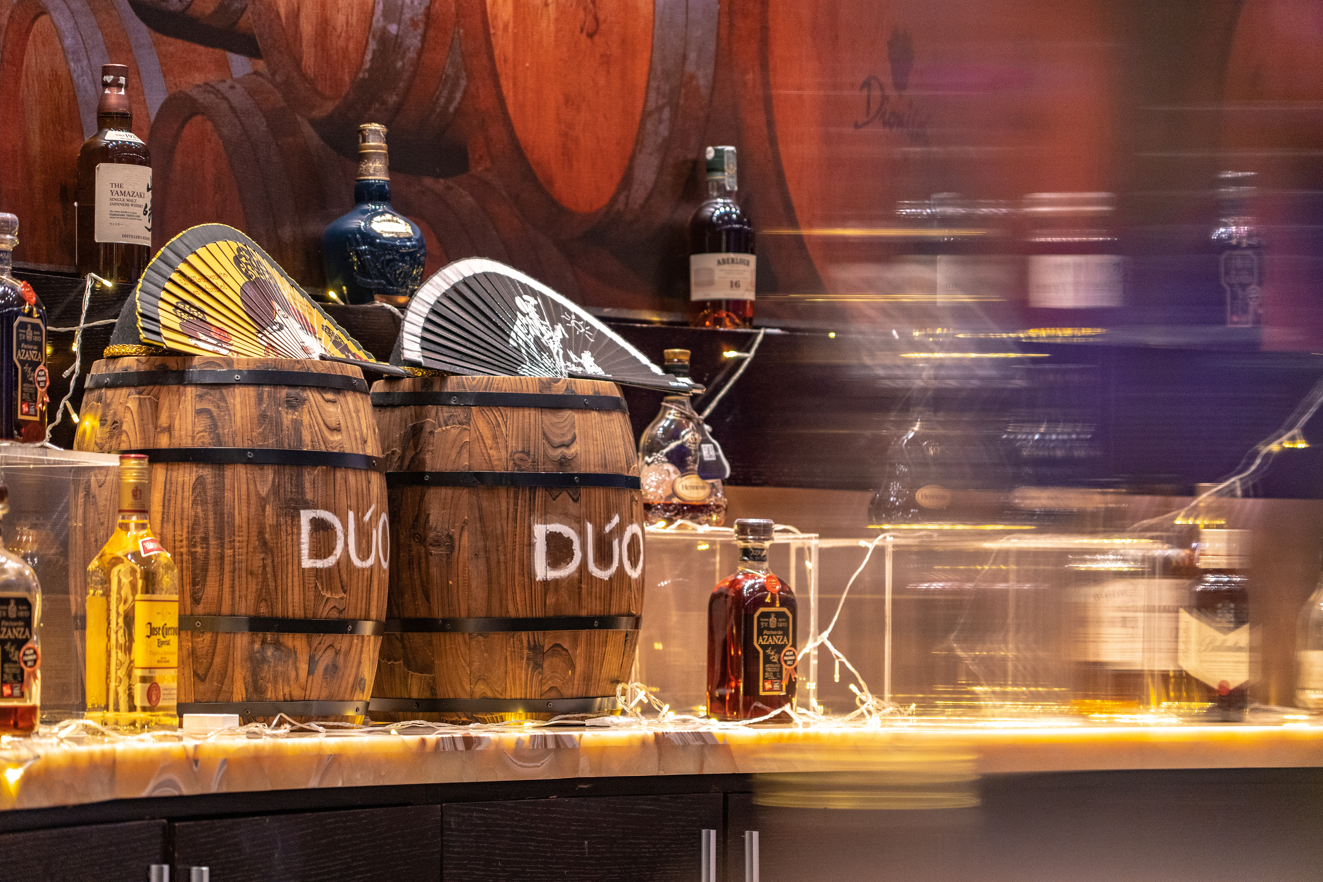 Spirits bottles (Yamazaki, Royal Salute), fans on 'DUO' barrels, lit bar display.