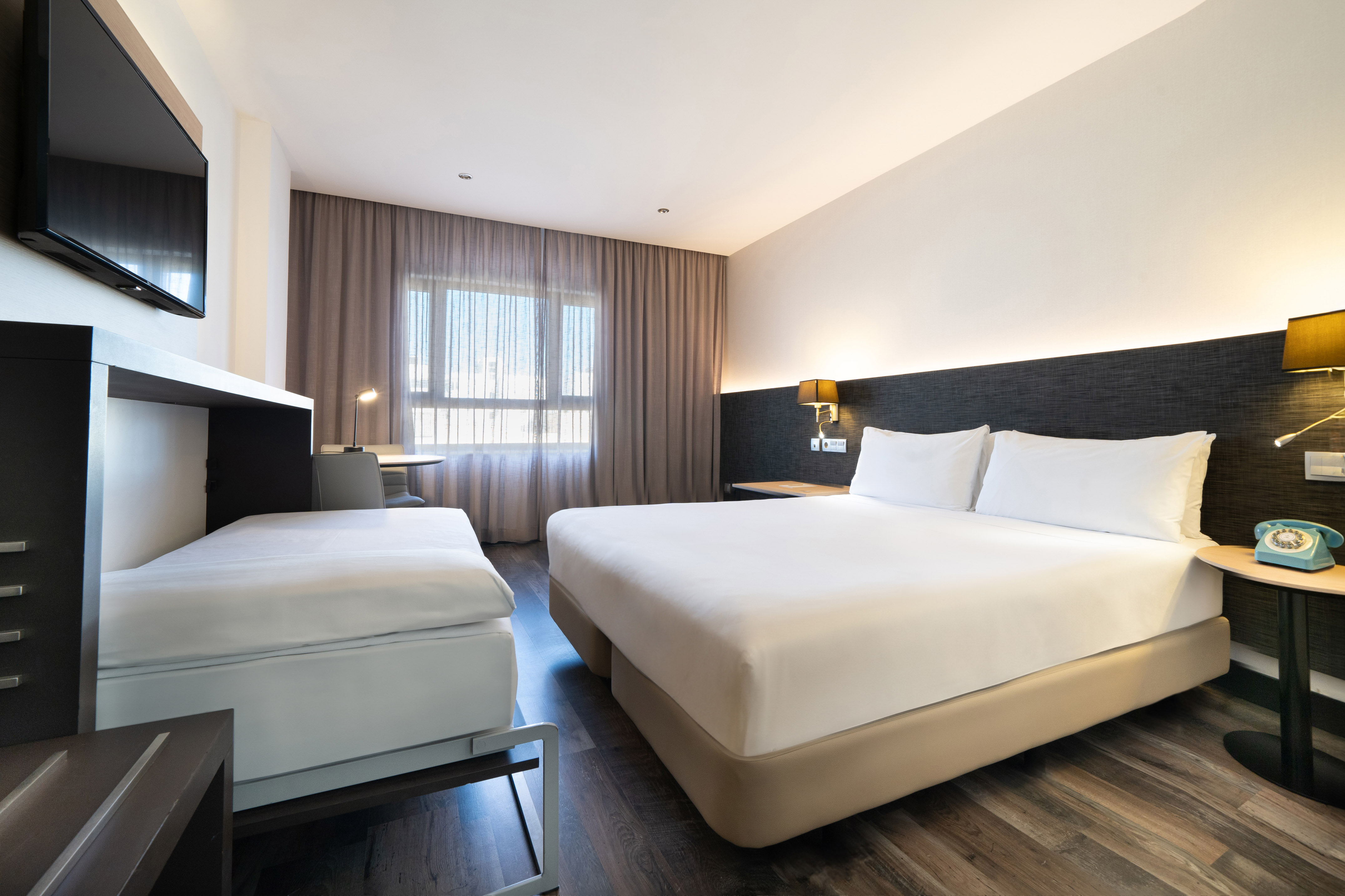 Modern hotel room with king bed, single pull-out bed, desk, and TV.