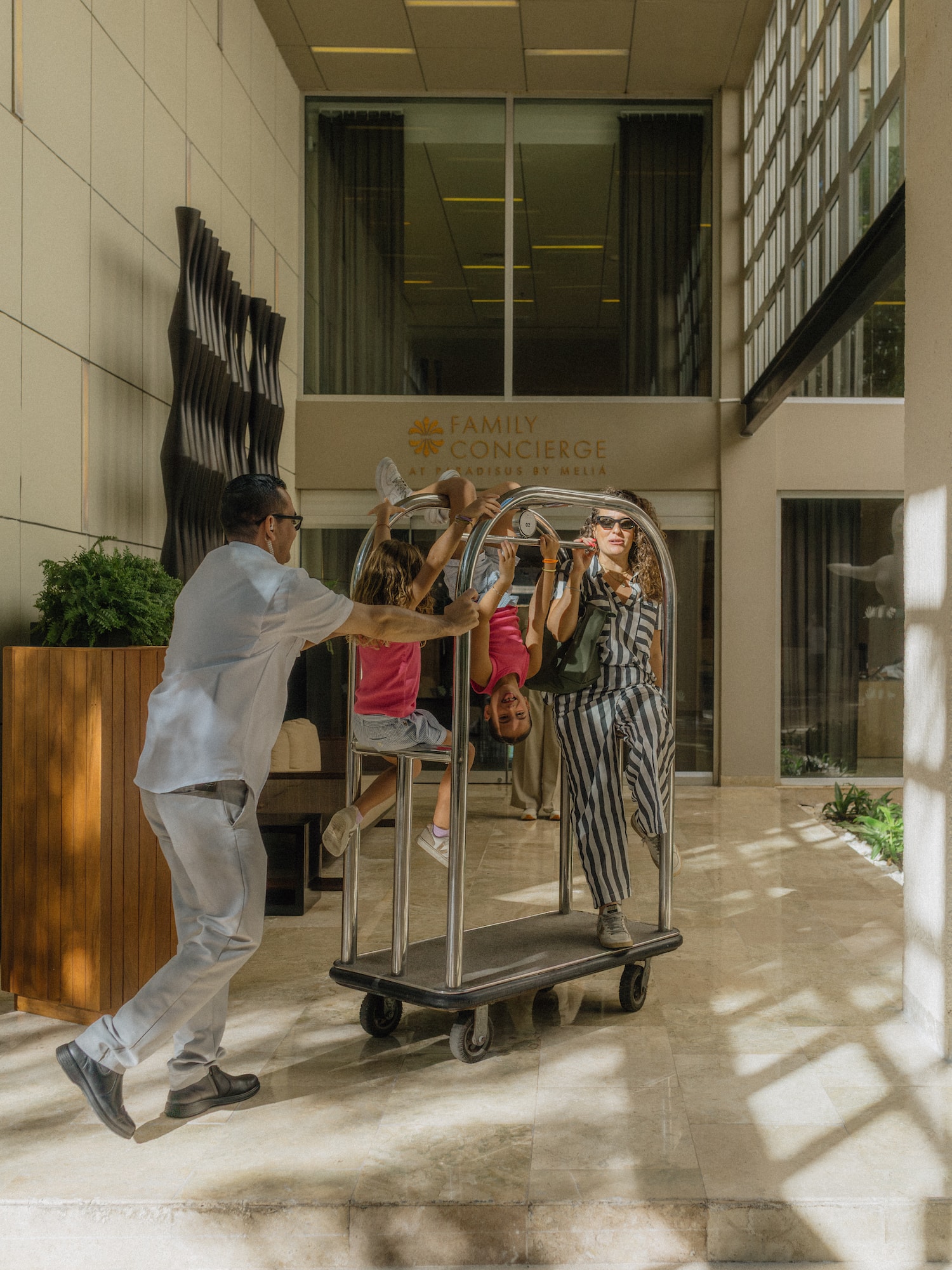 Playful family rides luggage cart with hotel bellboy, Meliá resort fun.