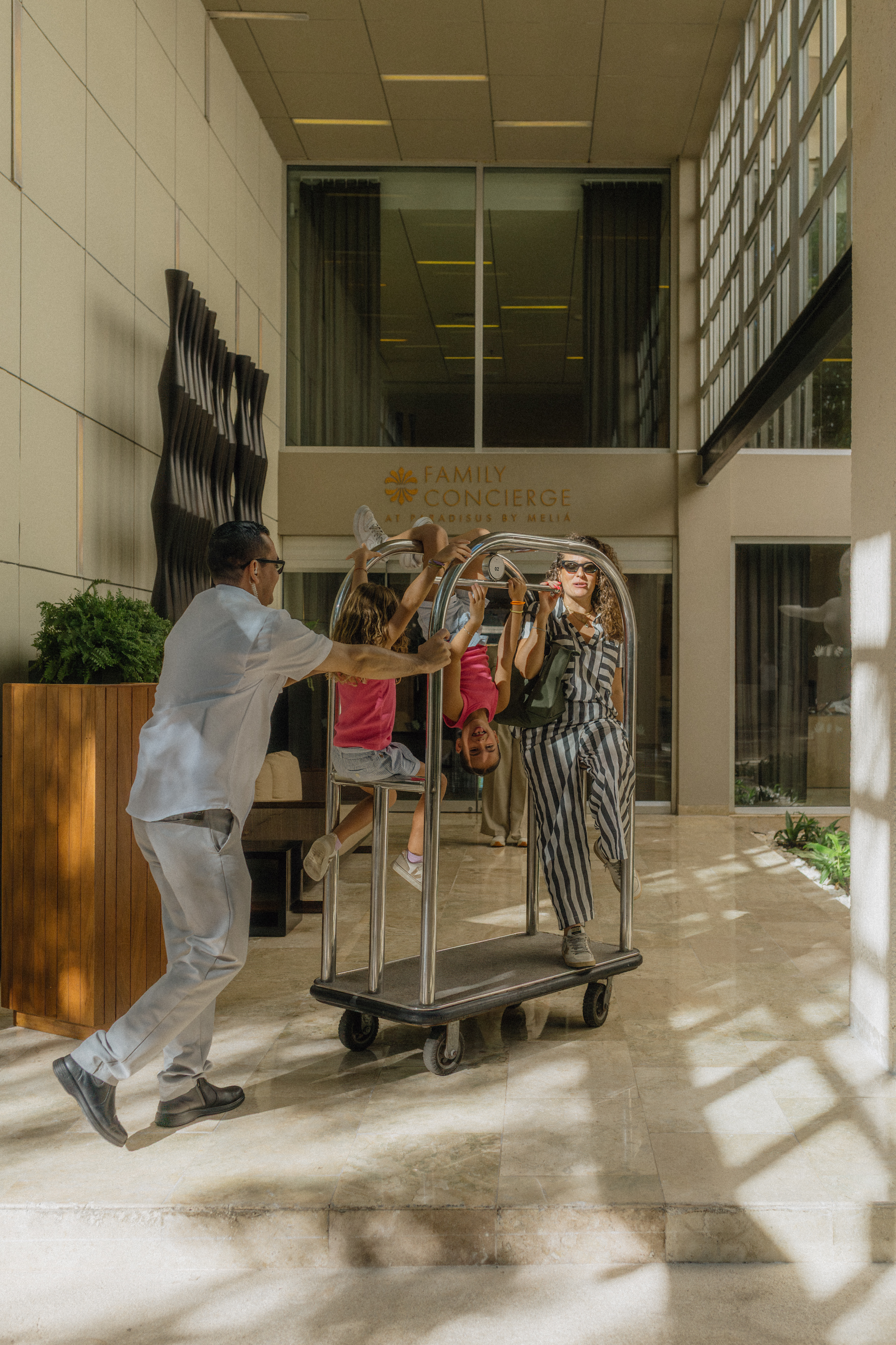 Playful family rides luggage cart with hotel bellboy, Meliá resort fun.