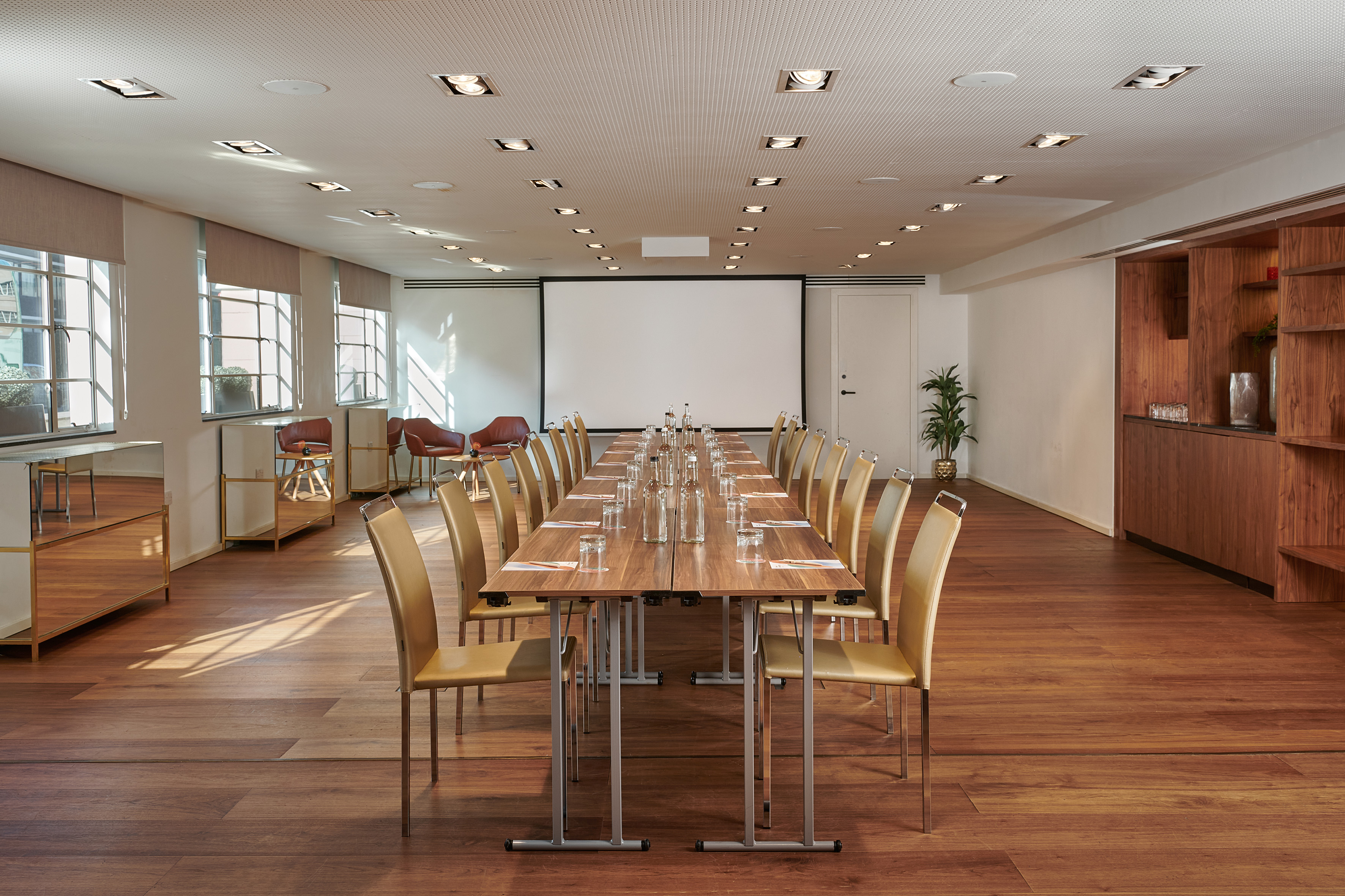 Modern meeting space with large conference table, beige chairs, and projector screen.