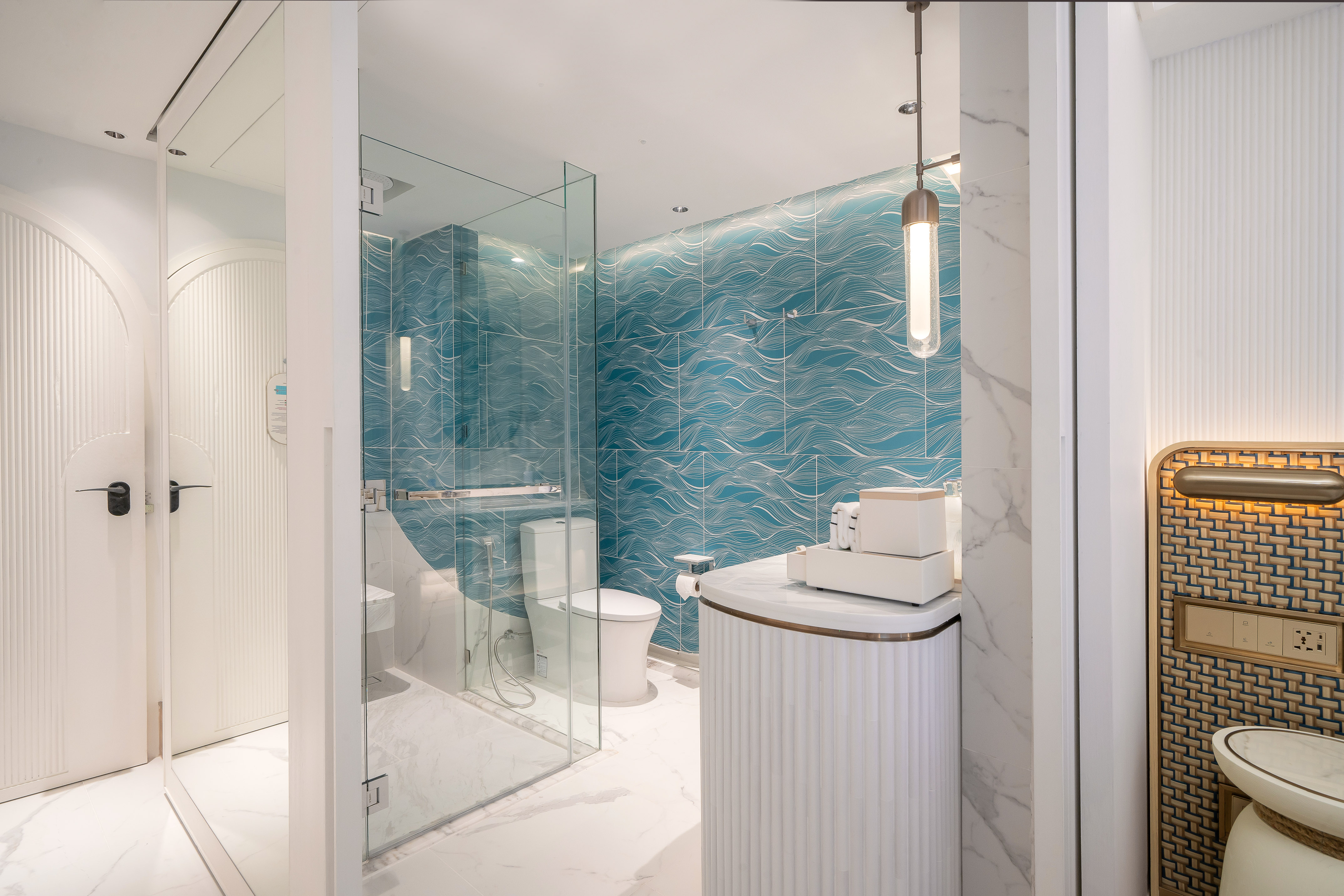 Modern bathroom with blue wave tiles, glass shower, and white fluted vanity.
