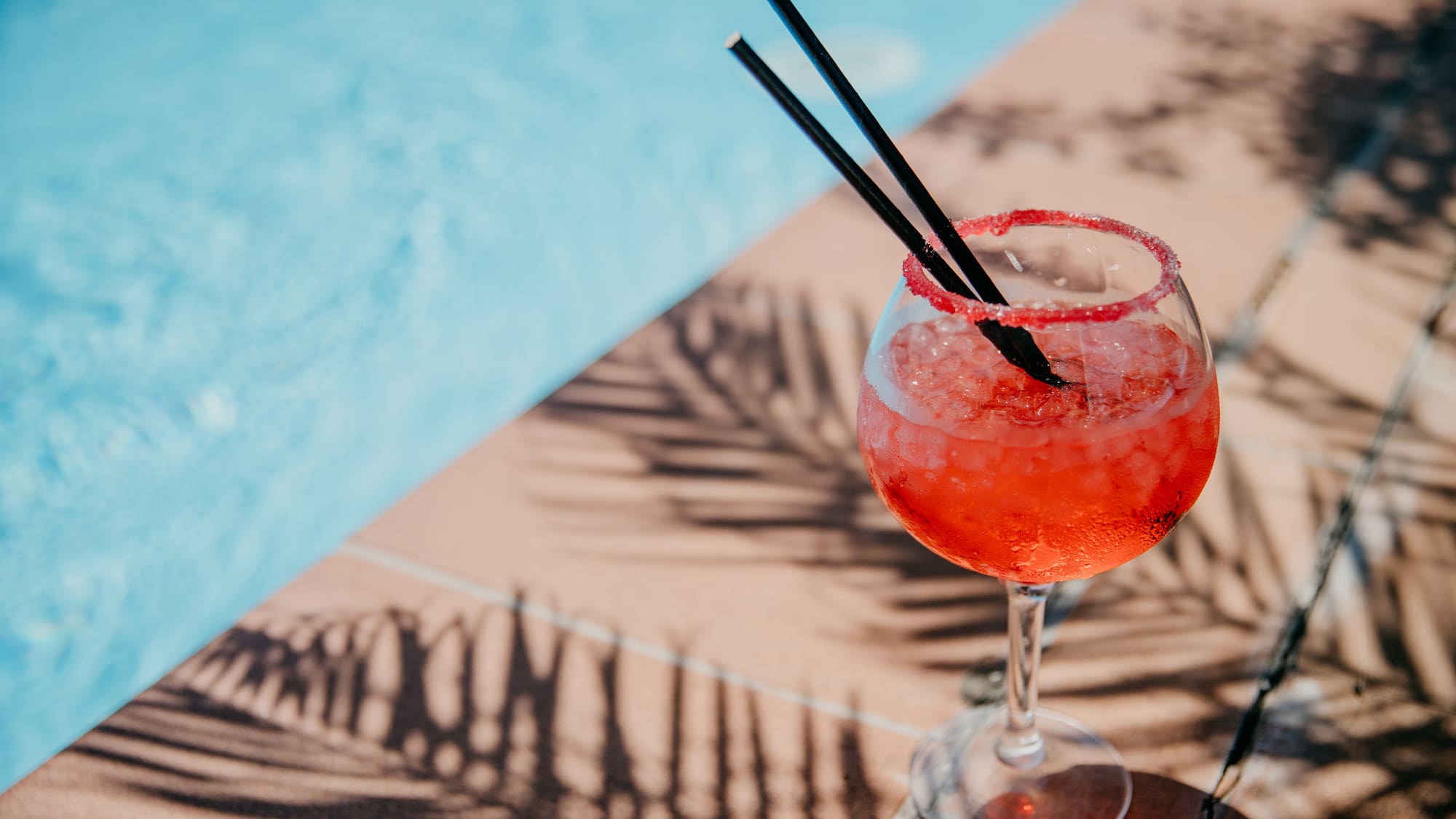 a glass of red liquid with straws on the edge of a pool