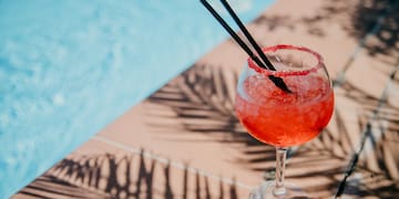 a glass of red liquid with straws on the edge of a pool
