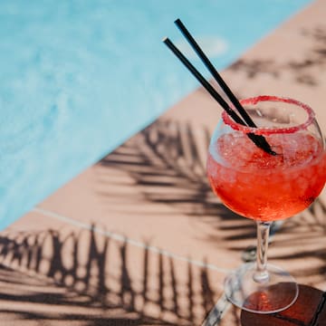 a glass of red liquid with straws on the edge of a pool