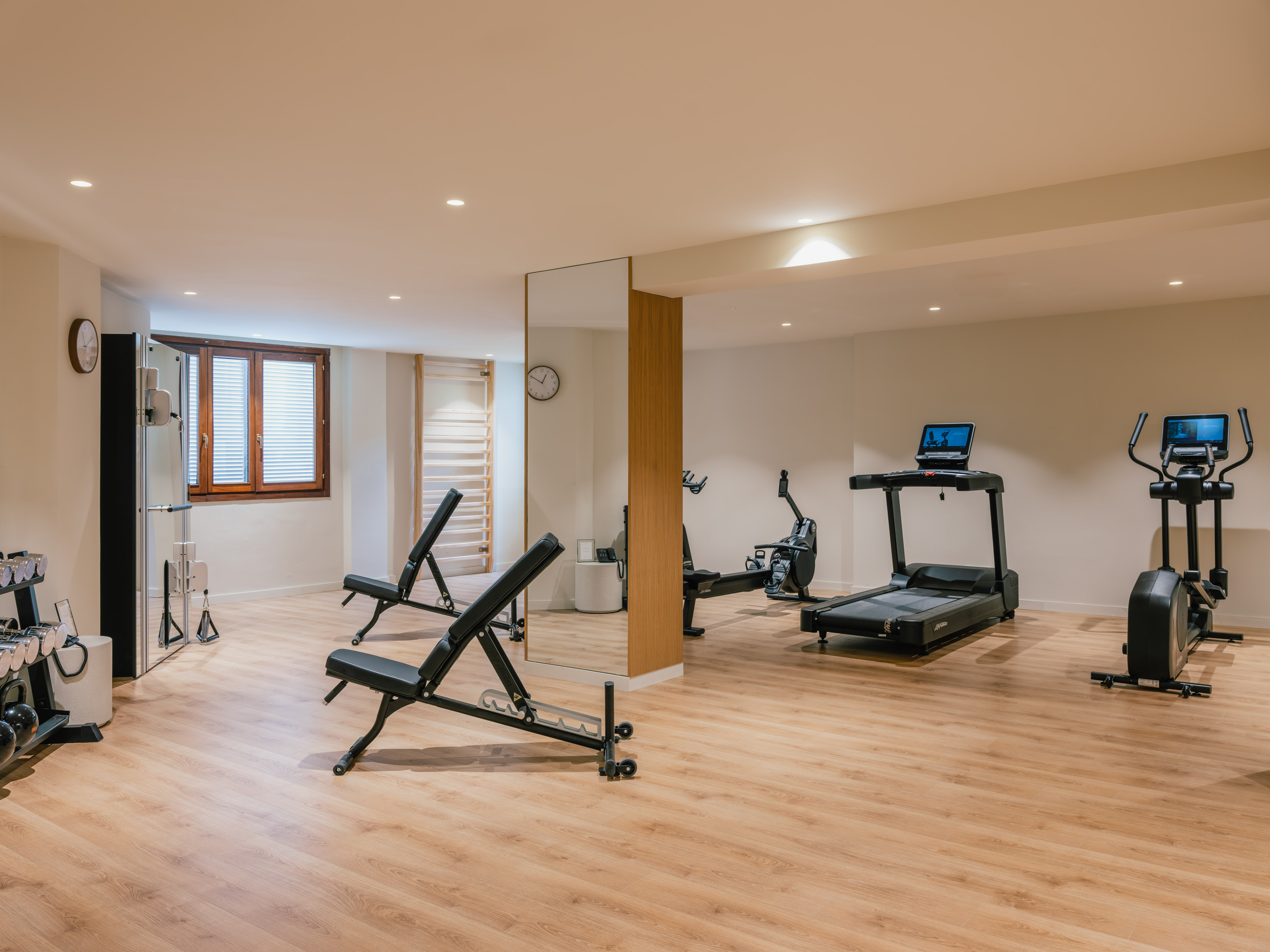 Modern fitness room with treadmill, elliptical, weights, and benches.