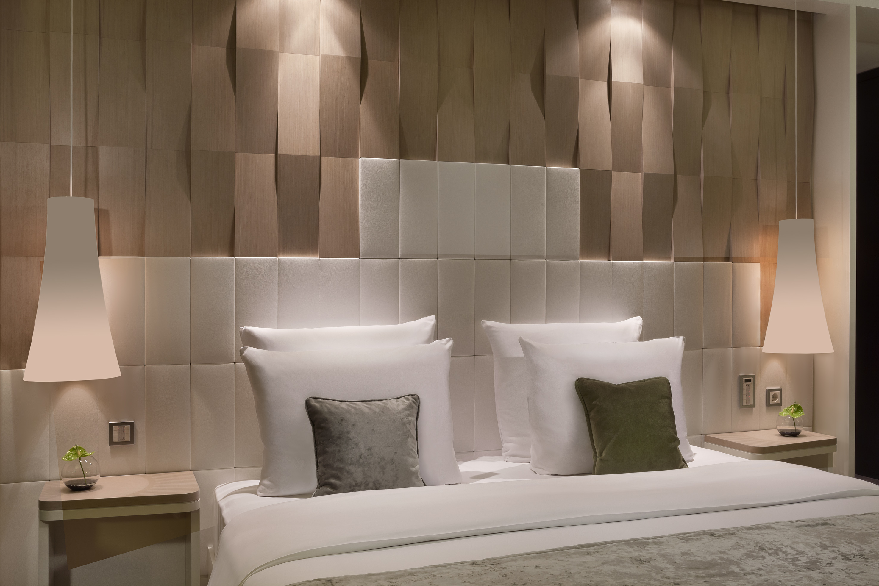 Elegant hotel bedroom: white bed, upholstered headboard, geometric wood wall.