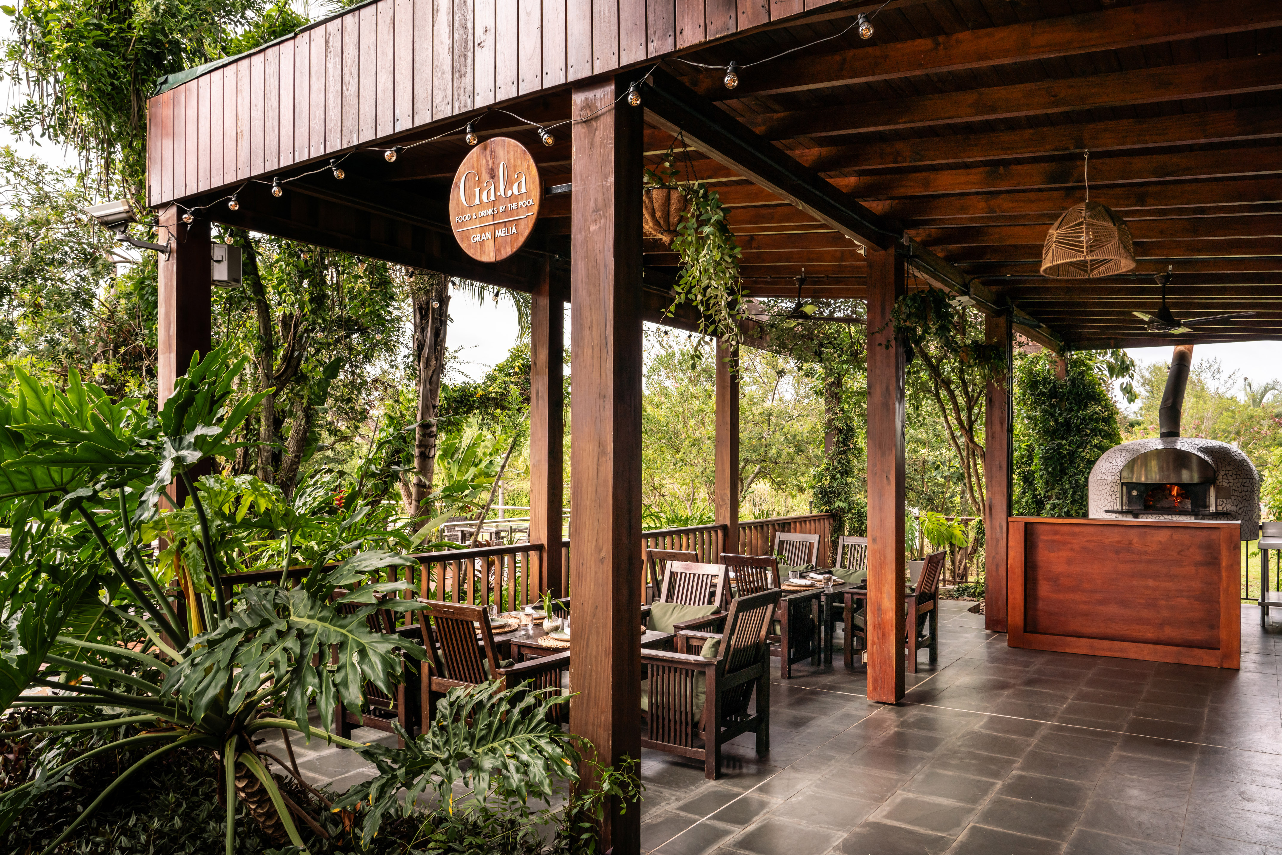 Gala Gran Meliá outdoor patio with tables, tropical plants, and pizza oven.